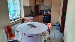 Une cuisine compacte avec des meubles de rangement en bois, un four à micro-ondes et un évier. On y trouve une table ronde avec des chaises et une fenêtre avec des rideaux.