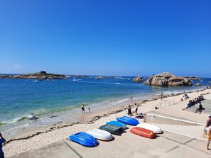 A beach with clear blue water, rocky outcrops, and several inflatable boats on the sand.