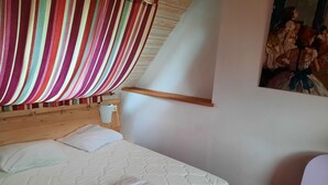 Un lit avec un matelas et des oreillers blancs, une tête de lit en bois, un rideau à rayures et un tableau accroché au mur.