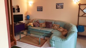 Un salon avec un canapé de couleur turquoise, une table basse en verre, un téléviseur et des lampes fixées au mur.