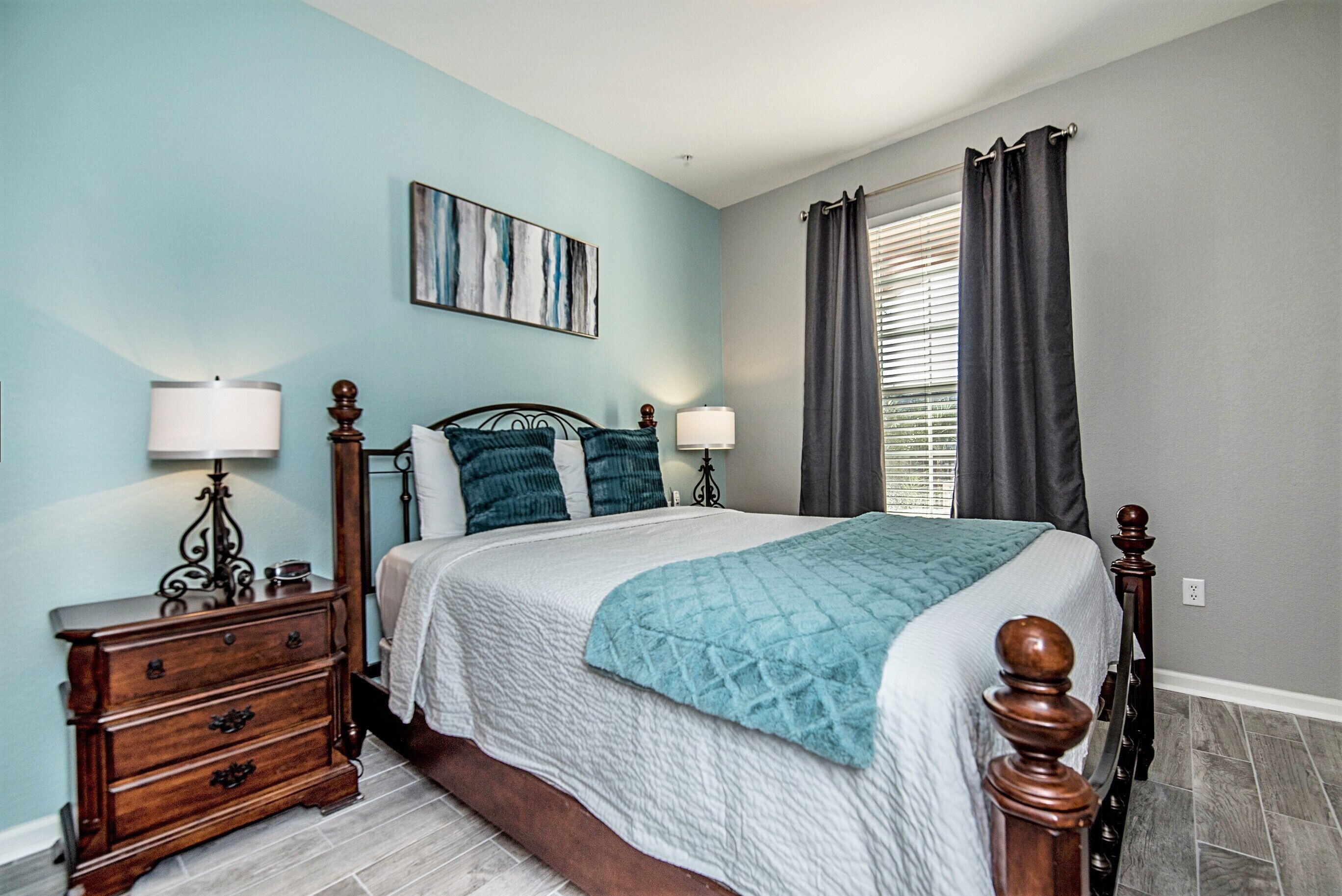 A bedroom with a bed, two bedside tables, a dresser, a painting on the wall, and a window with curtains.
