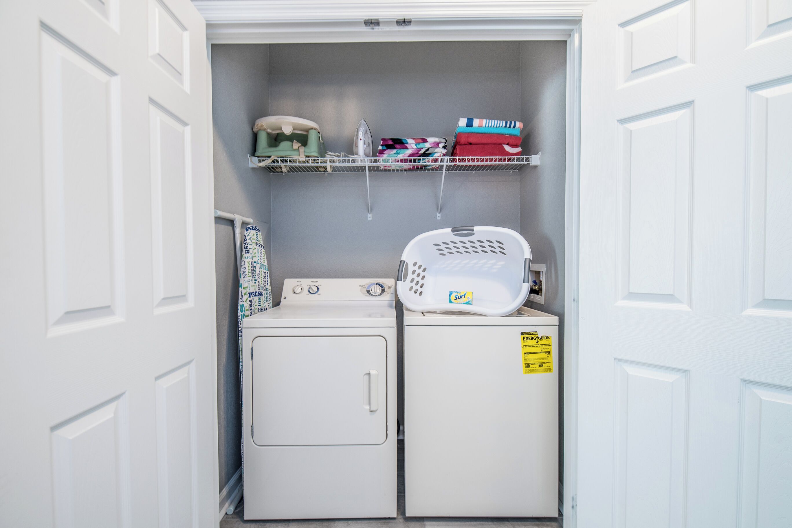 A laundry room with a washing machine, dryer, and a shelf with folded clothes and an iron.