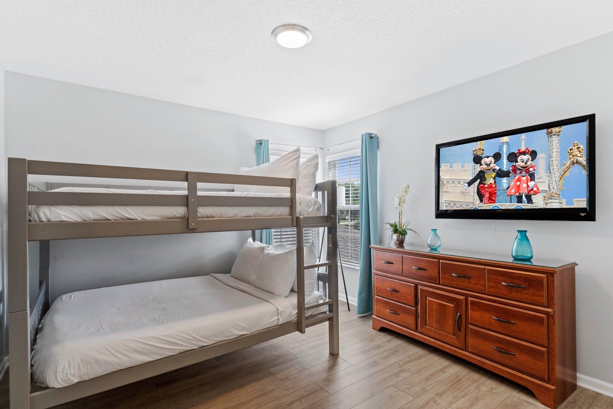 Une chambre avec un lit superposé, une commode en bois et un téléviseur diffusant des dessins animés.
