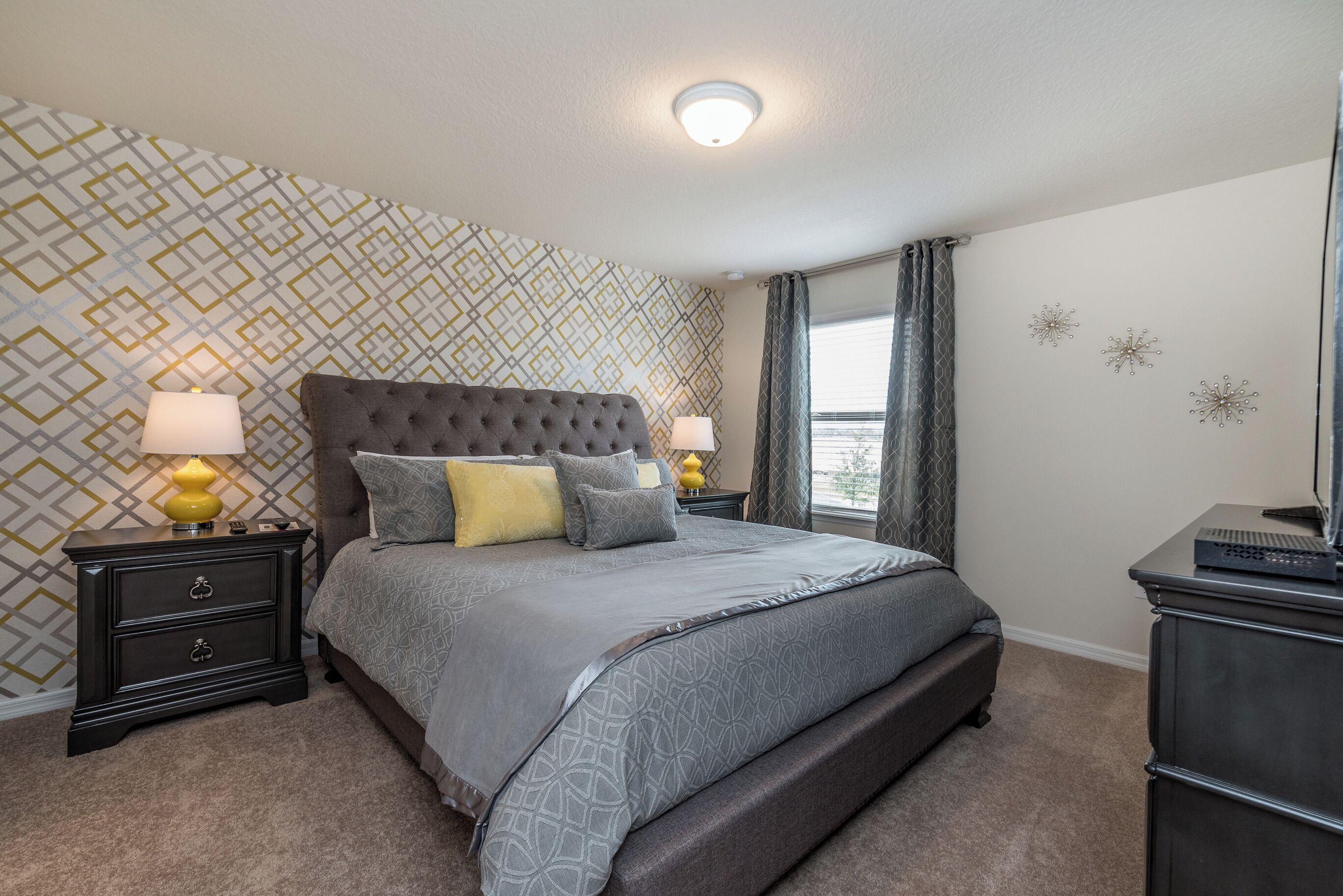 A bedroom with a large bed, two bedside tables with lamps, a dresser, and a patterned wallpaper.