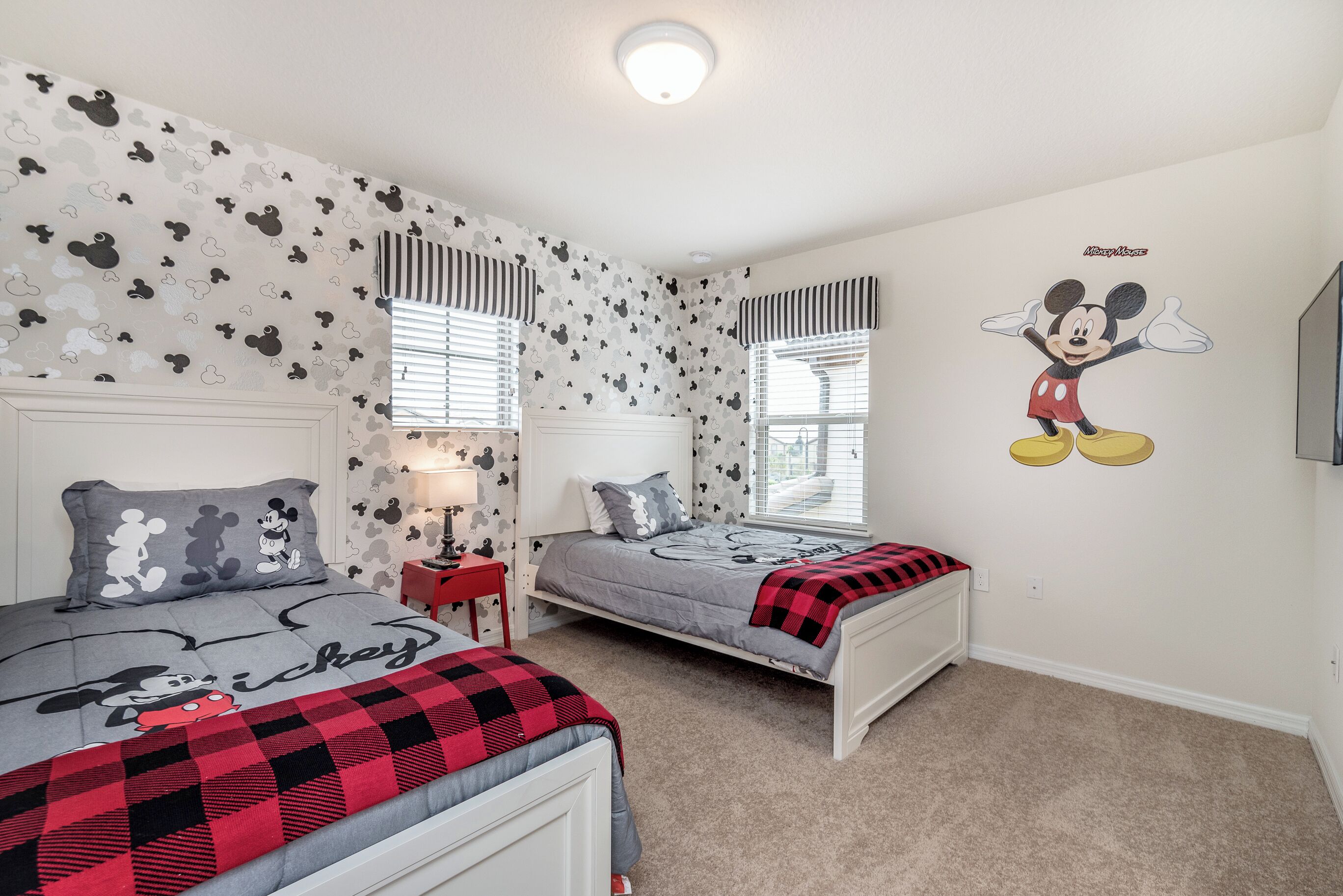 A bedroom with two beds, Mickey Mouse wall decal, and striped window valances.
