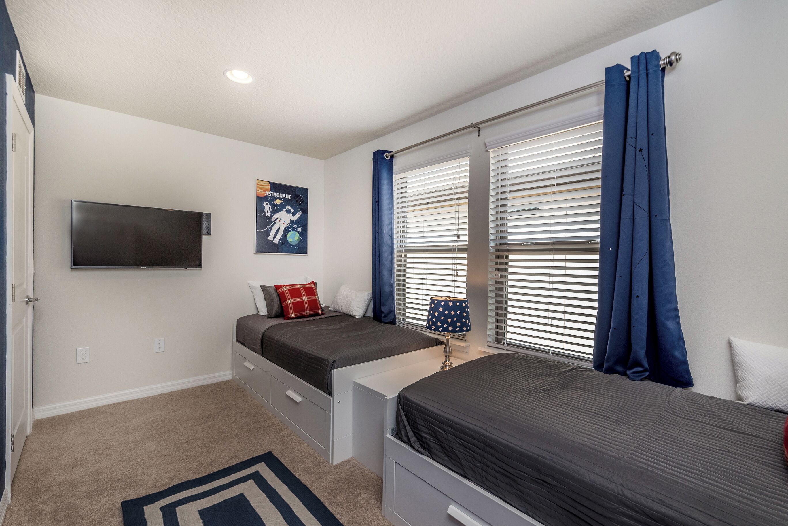 A bedroom with two beds, a TV mounted on the wall, and a poster of astronauts.