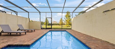 A swimming pool with a clear view of the sky and a brick pathway.