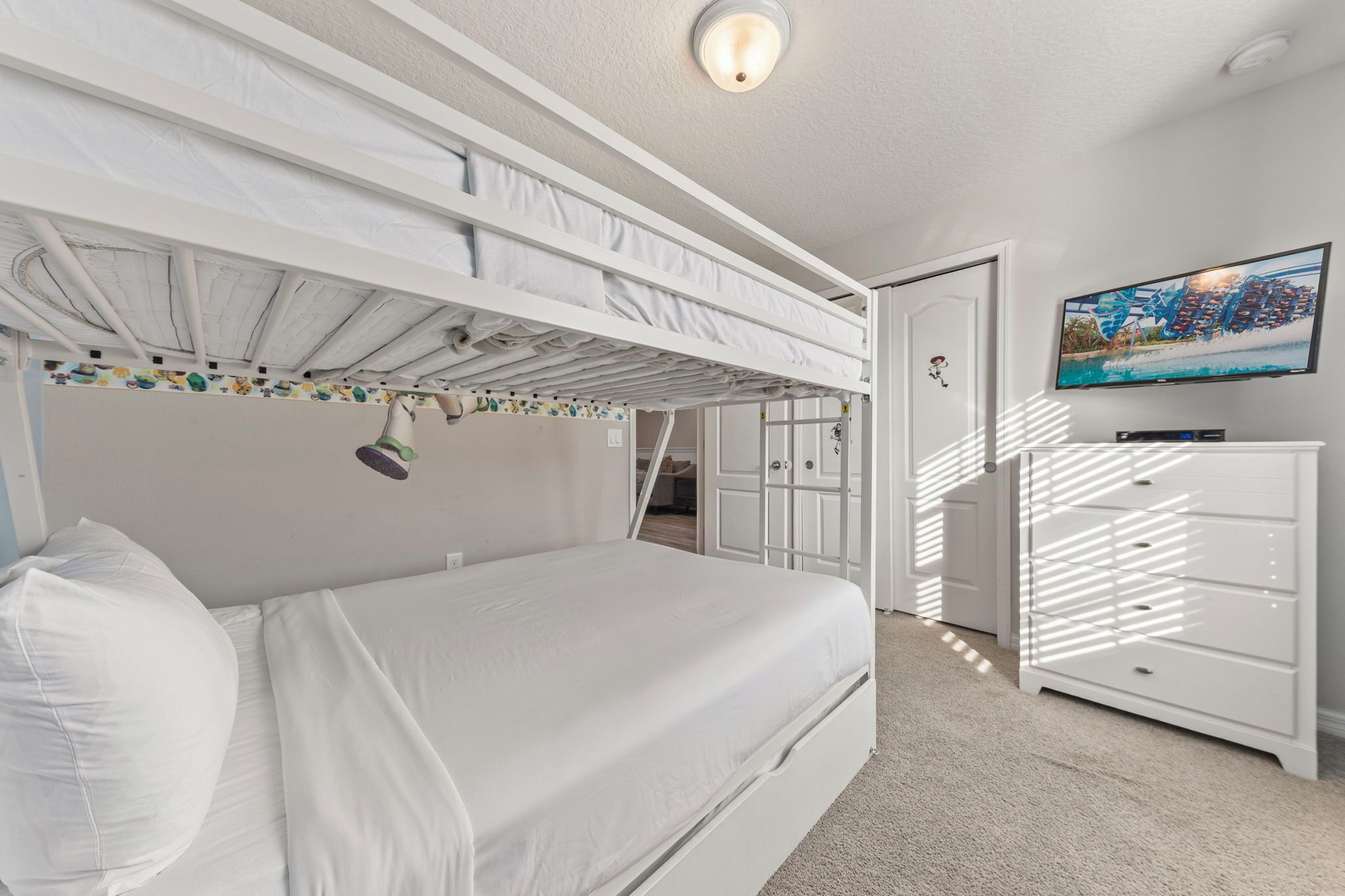A bedroom with a bunk bed, a desk, a dresser, and a television.