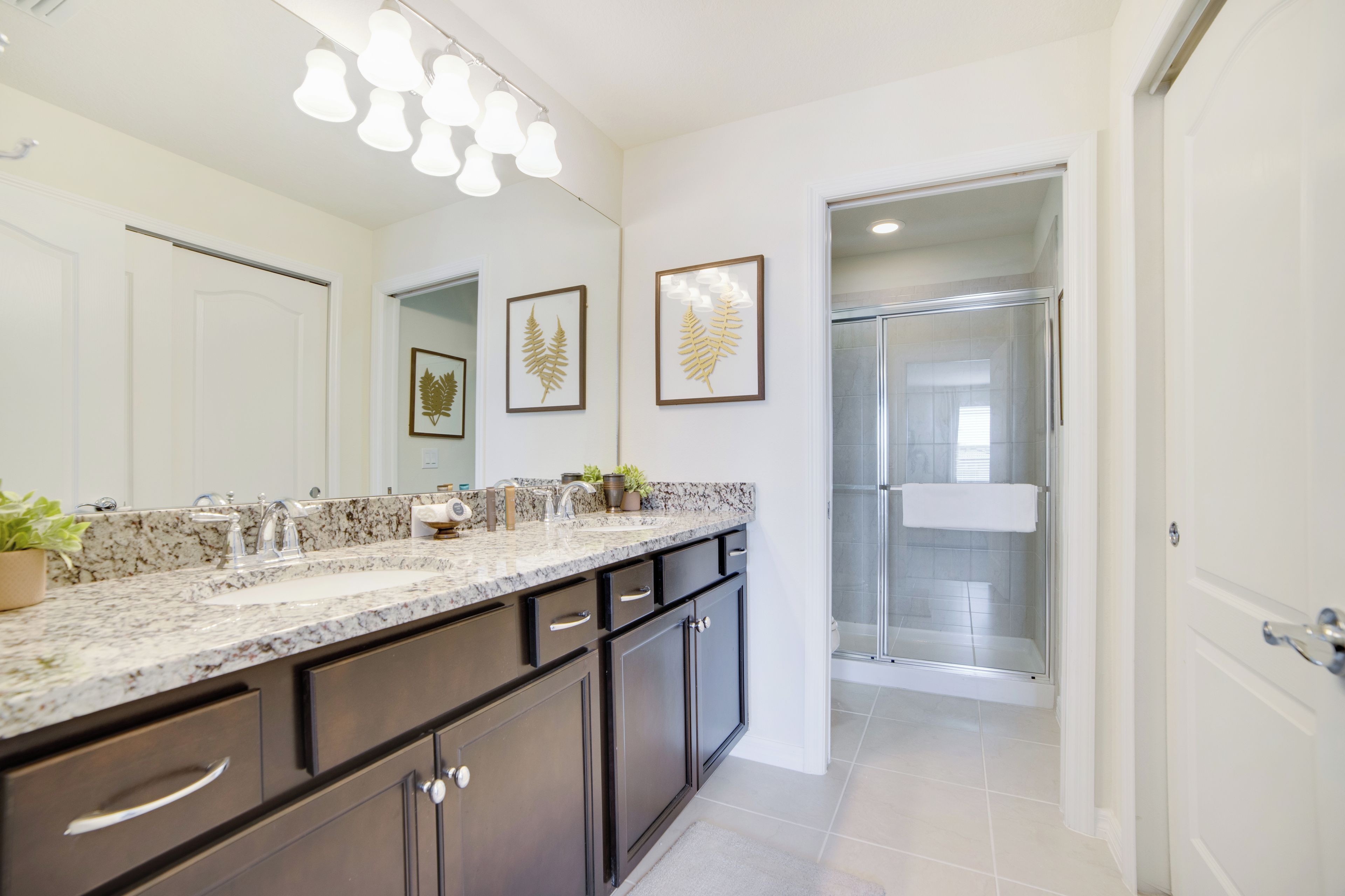 A modern bathroom with a large mirror, granite countertop, dark cabinets, and a glass shower enclosure.