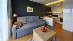Ein modernes Wohnzimmer mit einem grauen Sofa, einem Couchtisch mit Äpfeln und einer Küche im Hintergrund.
