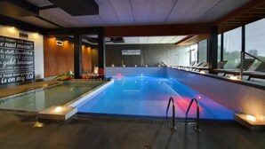 Ein moderner, überdachter Pool mit Blick ins Freie, eine Schilderung von Wellness- und Spa-Angeboten sowie ein Poolbereich mit Liegestühlen.