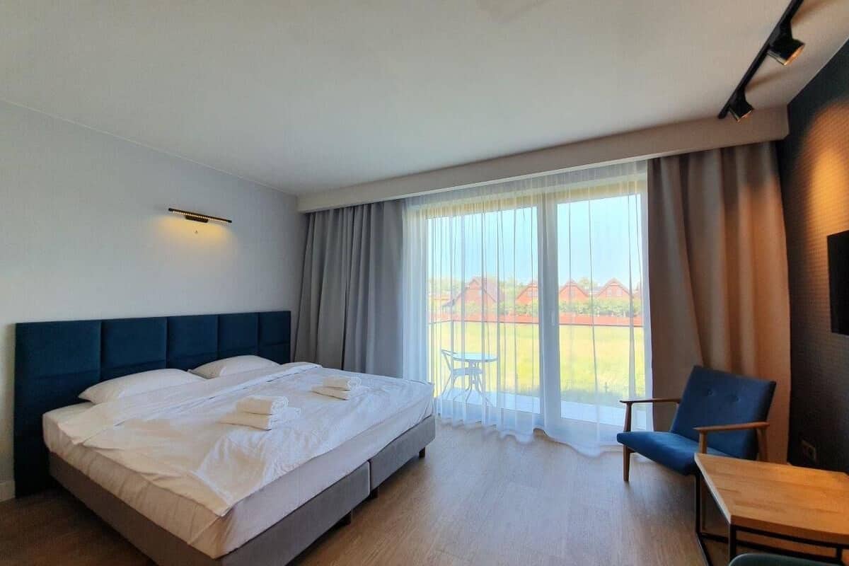 A hotel room with a large bed, a small table, a chair, and a balcony with a view.