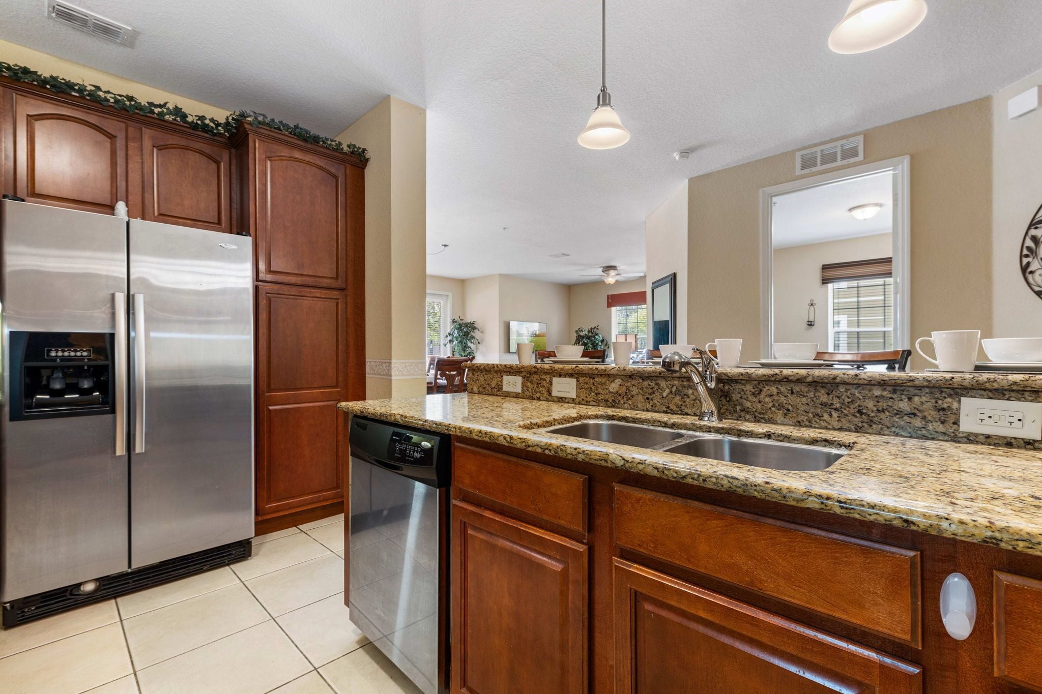A kitchen with wooden cabinets, a stainless steel refrigerator, a dishwasher, granite countertops, and a double sink.