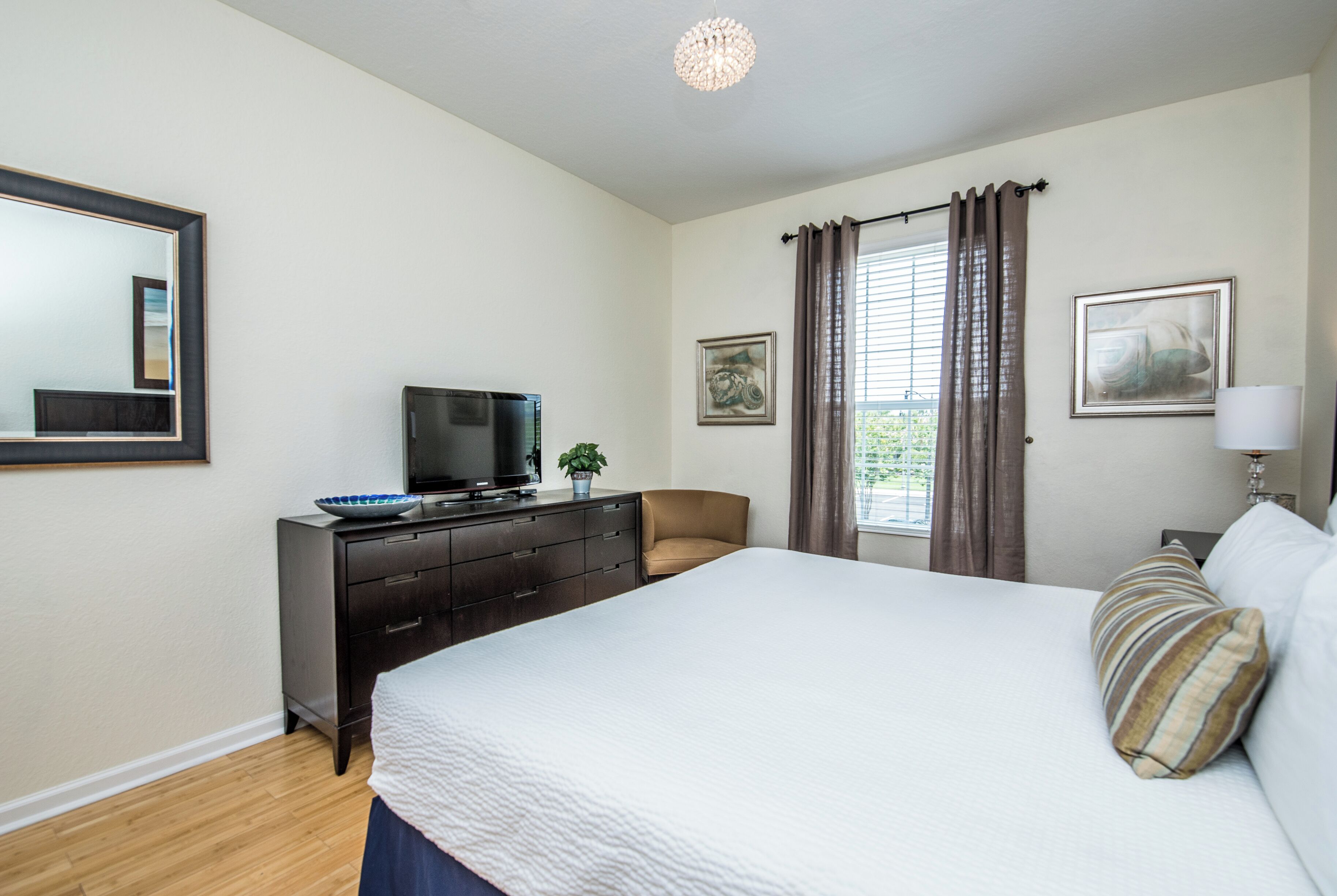 A bedroom with a large bed, a dresser, a television, and a window with curtains.