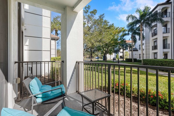 A balcony with a seating area, a small table, and a view of a well-maintained garden and buildings in the background. - Cozy Escape (Orlando)