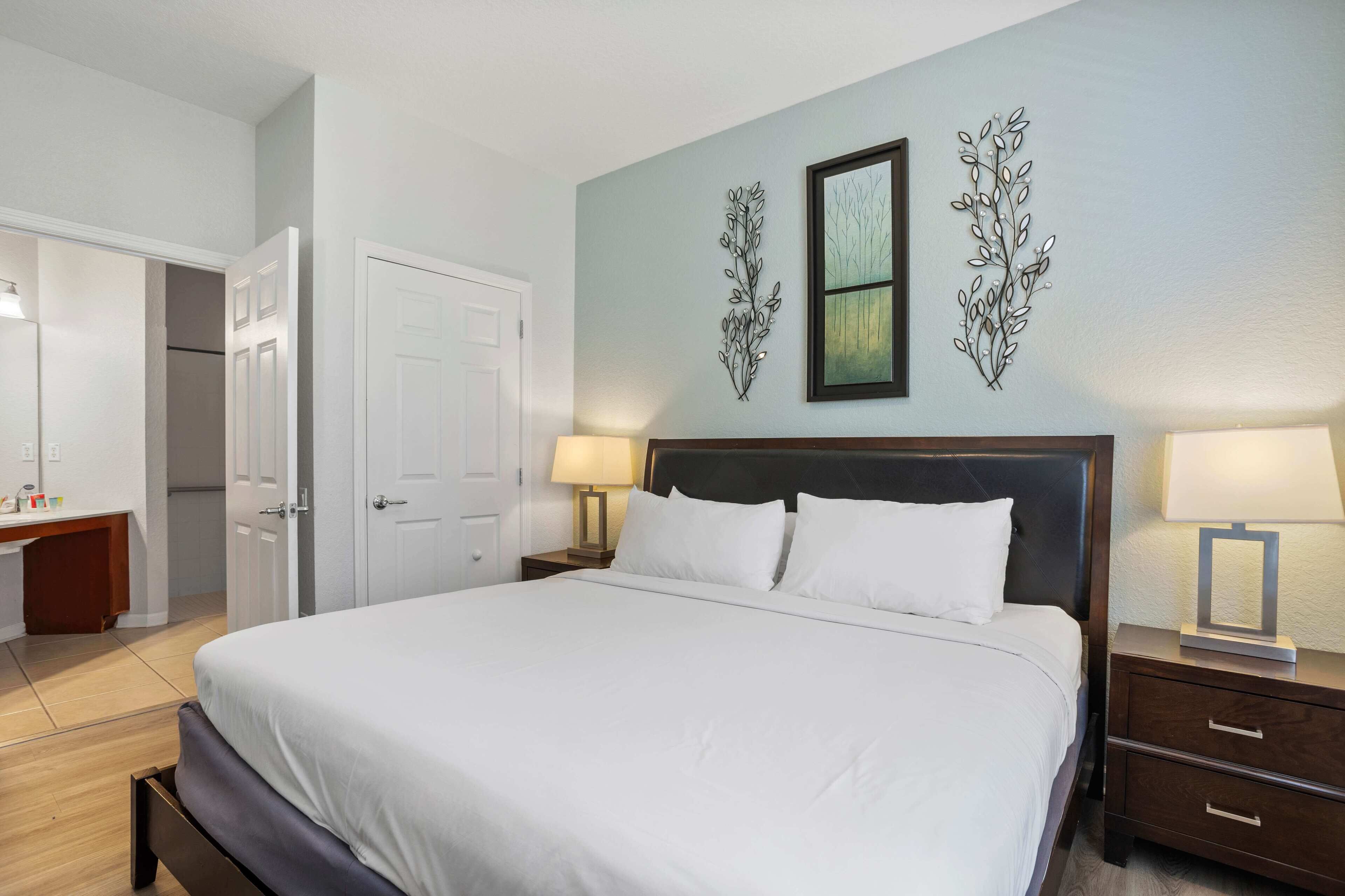 A neatly made bed in a hotel room with a large mirror, a bedside table with a lamp, and a wardrobe.