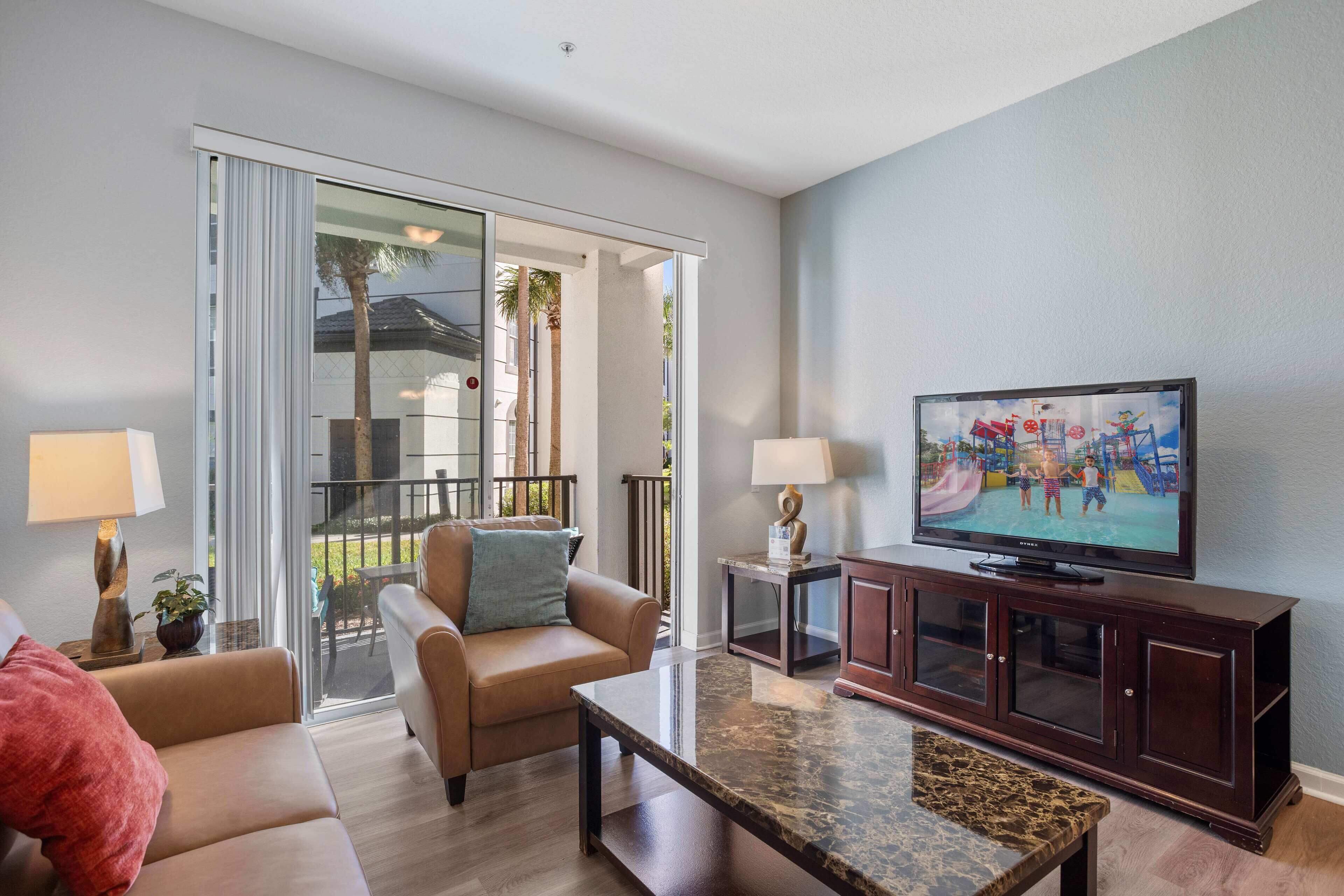 A living room with a sofa, a coffee table, a TV, and a sliding glass door leading to a balcony.