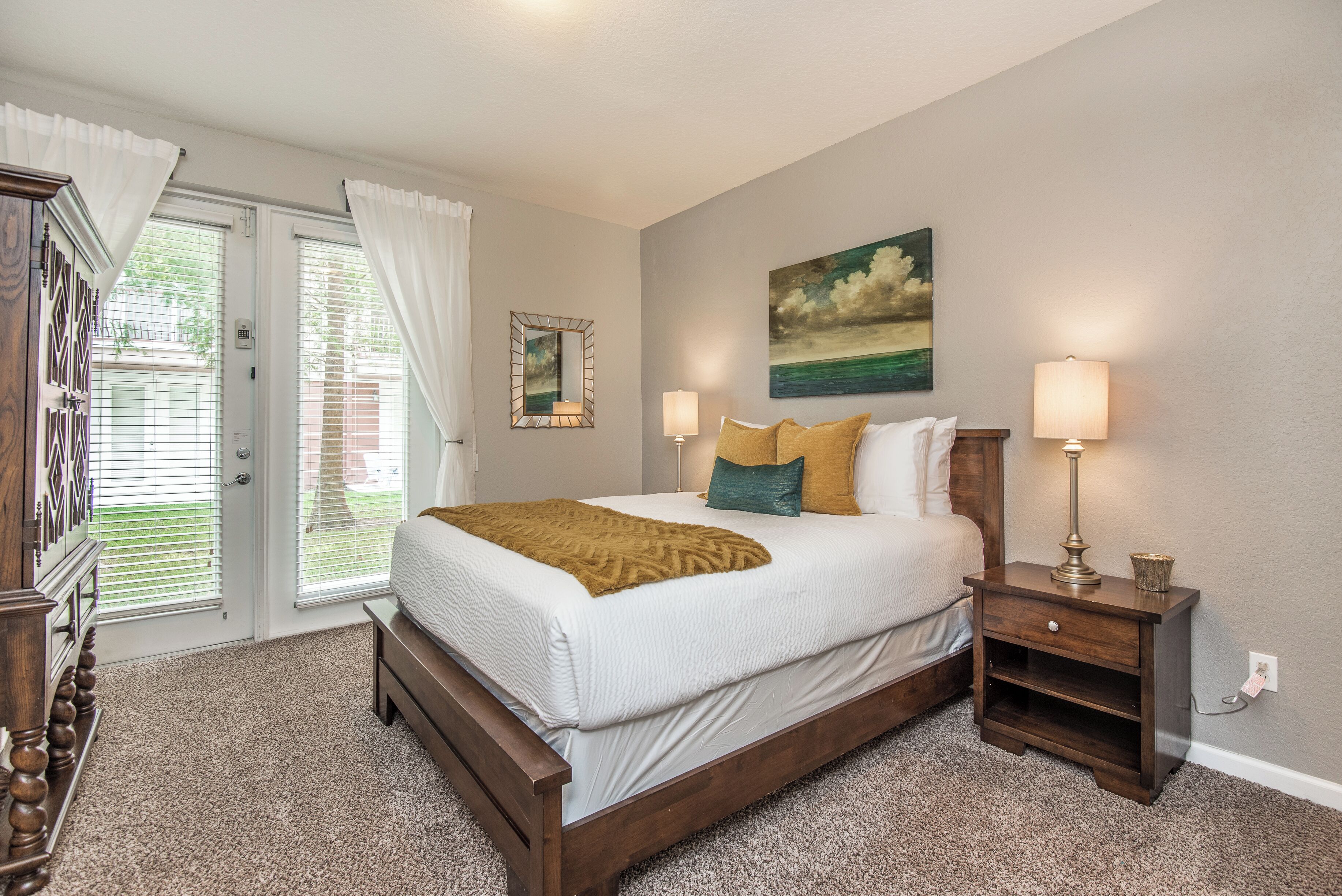A bedroom with a bed, bedside lamps, a nightstand, a mirror, and a painting on the wall.