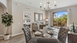 A modern living room with a dining area, a chandelier, a large potted plant, and a balcony with a view.
