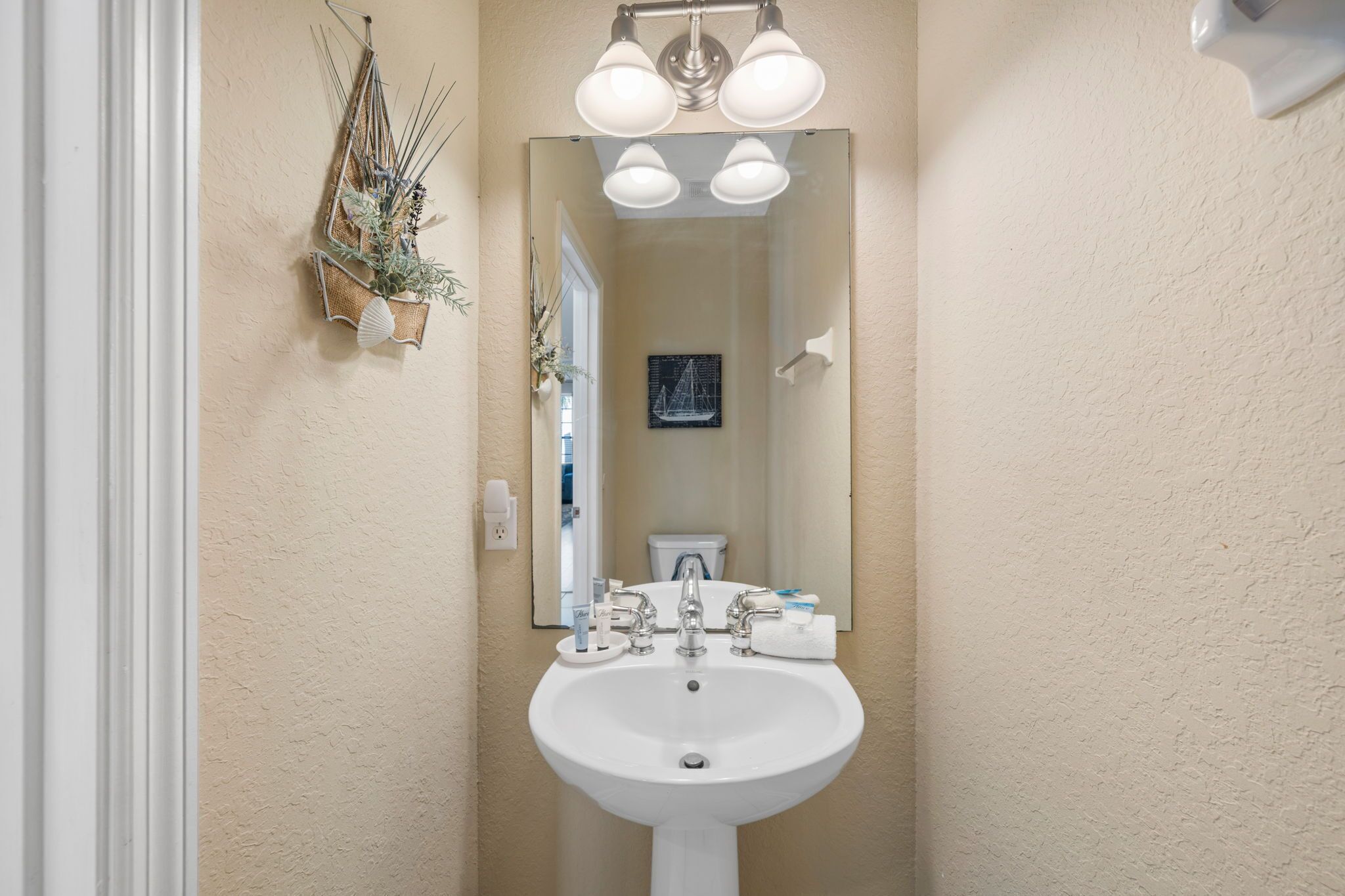 A bathroom with a white sink, three light fixtures above it, a mirror, and a wall-mounted plant.
