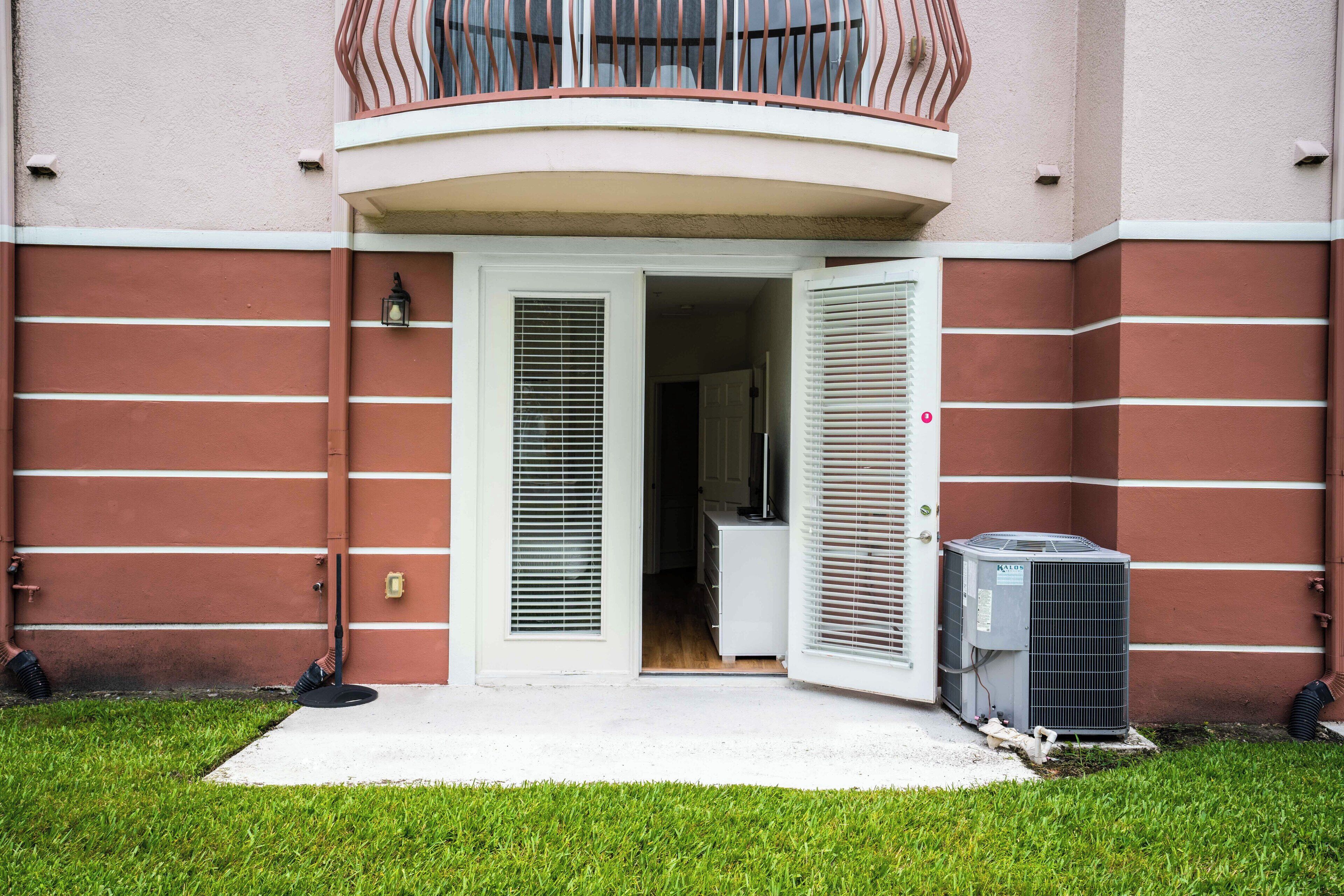 A building entrance with a white door, a small balcony with a metal railing, and an air conditioning unit outside.