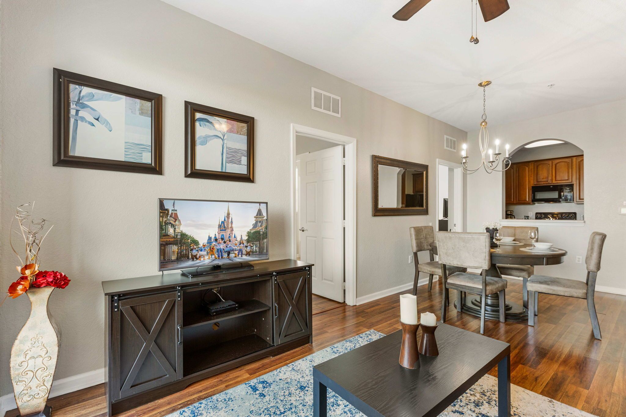 A living room with a TV, entertainment center, dining area, kitchen, and ceiling fan.