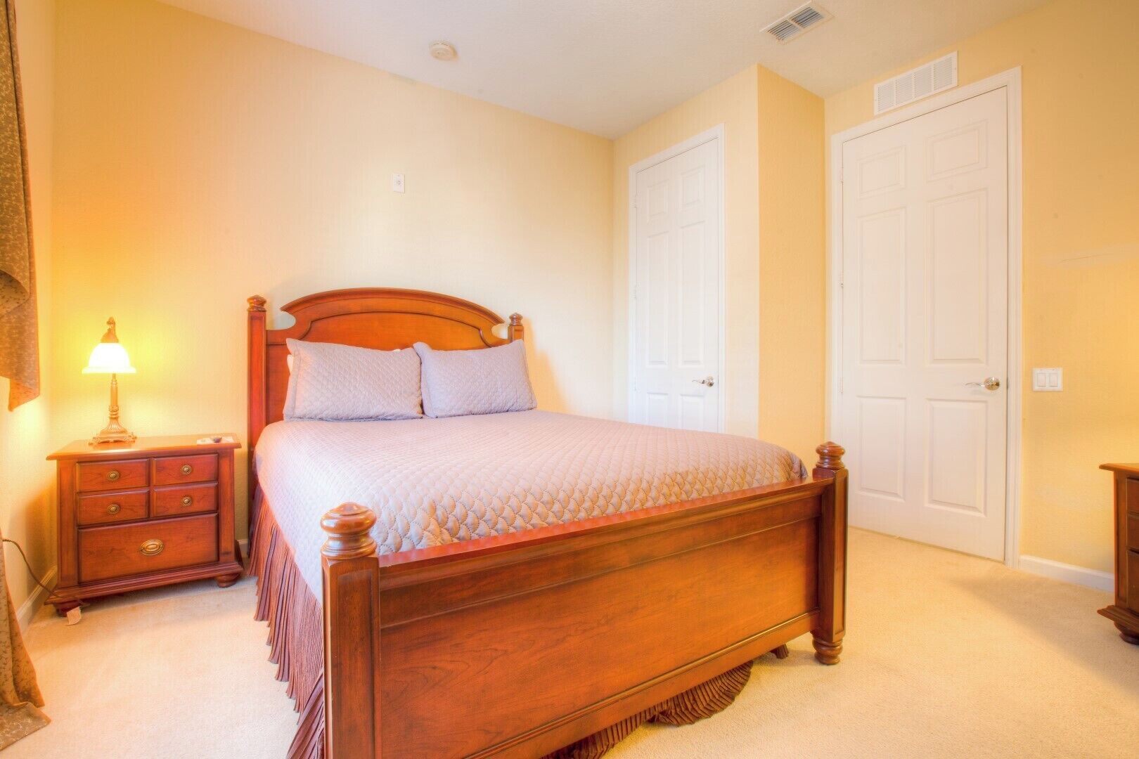 A bedroom with a wooden bed, a nightstand with a lamp, and two white doors.