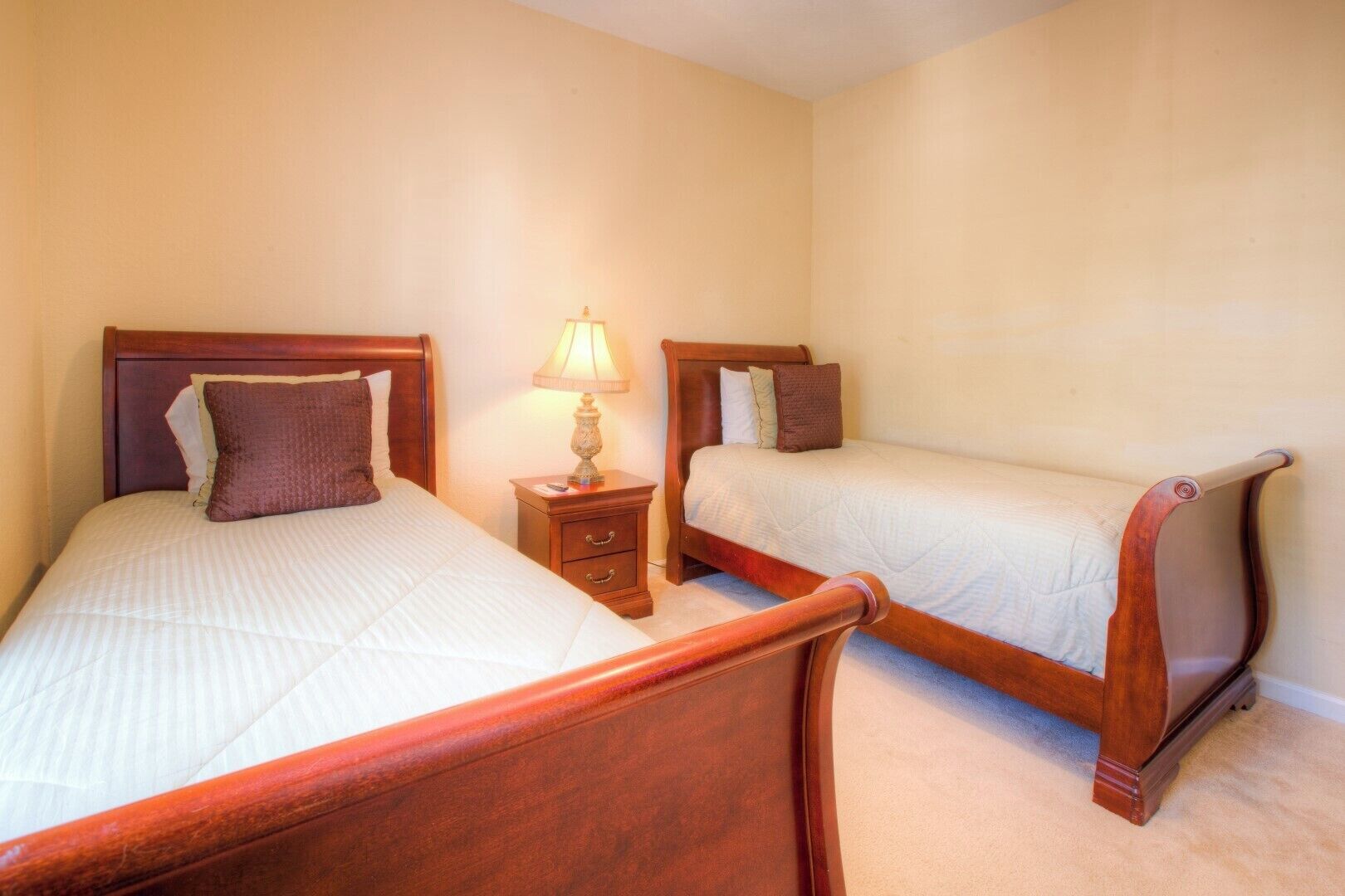 A bedroom with two single beds, a nightstand with a lamp, and a small drawer.