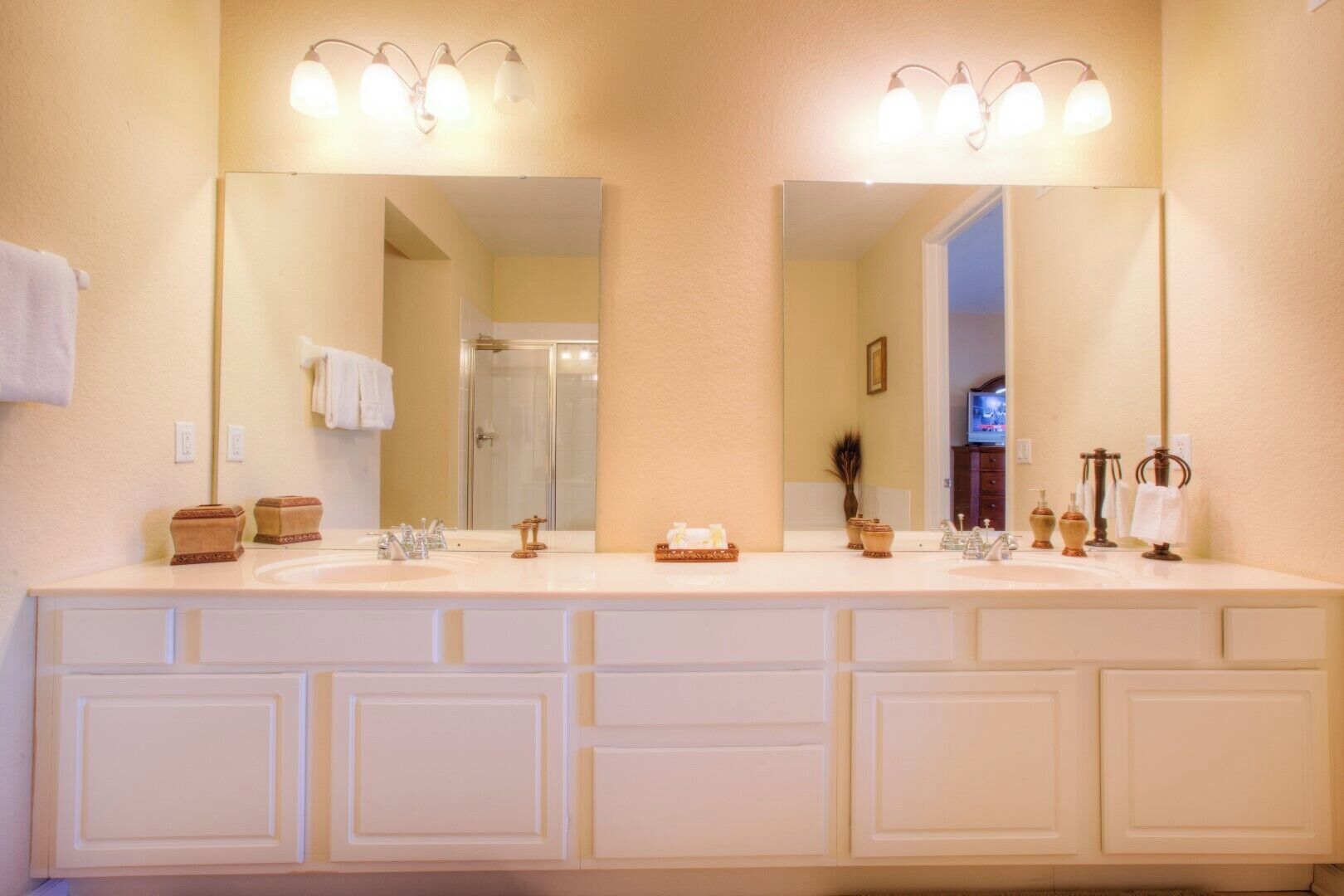 A bathroom with two sinks, a large mirror, and a shower visible in the background.