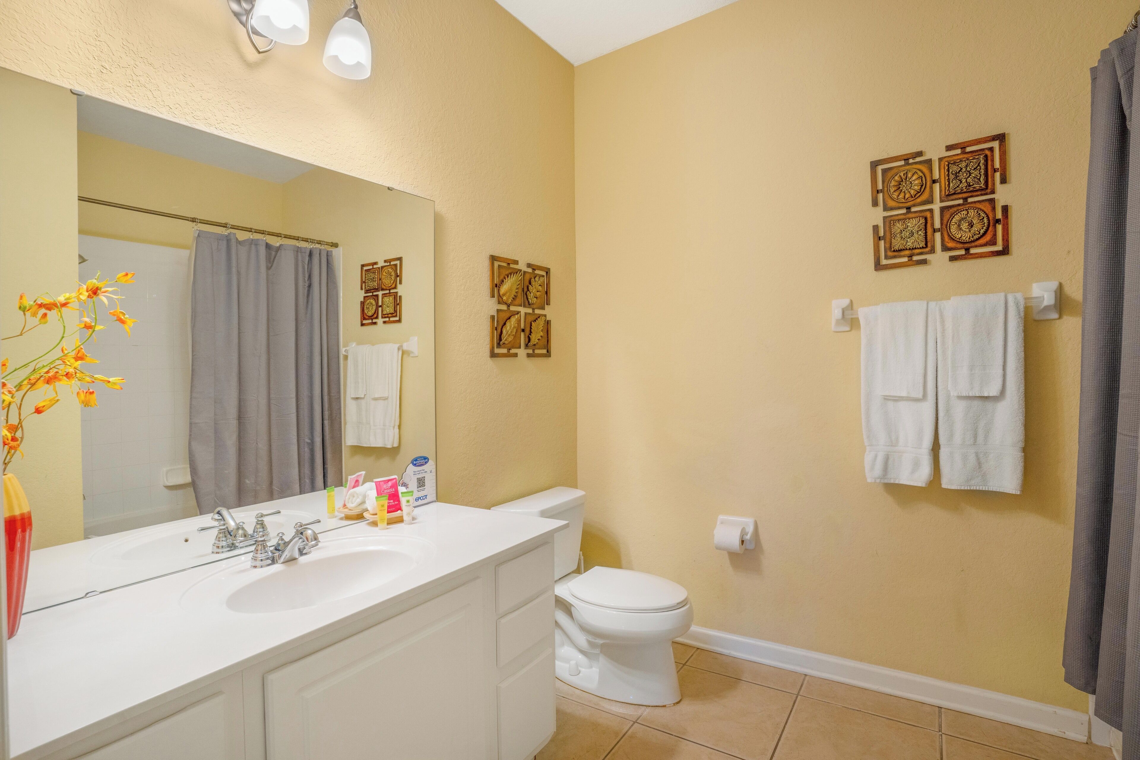 Une salle de bain avec un lavabo blanc, un miroir et des toilettes. Des serviettes sont accrochées au mur et il y a un rideau de douche.