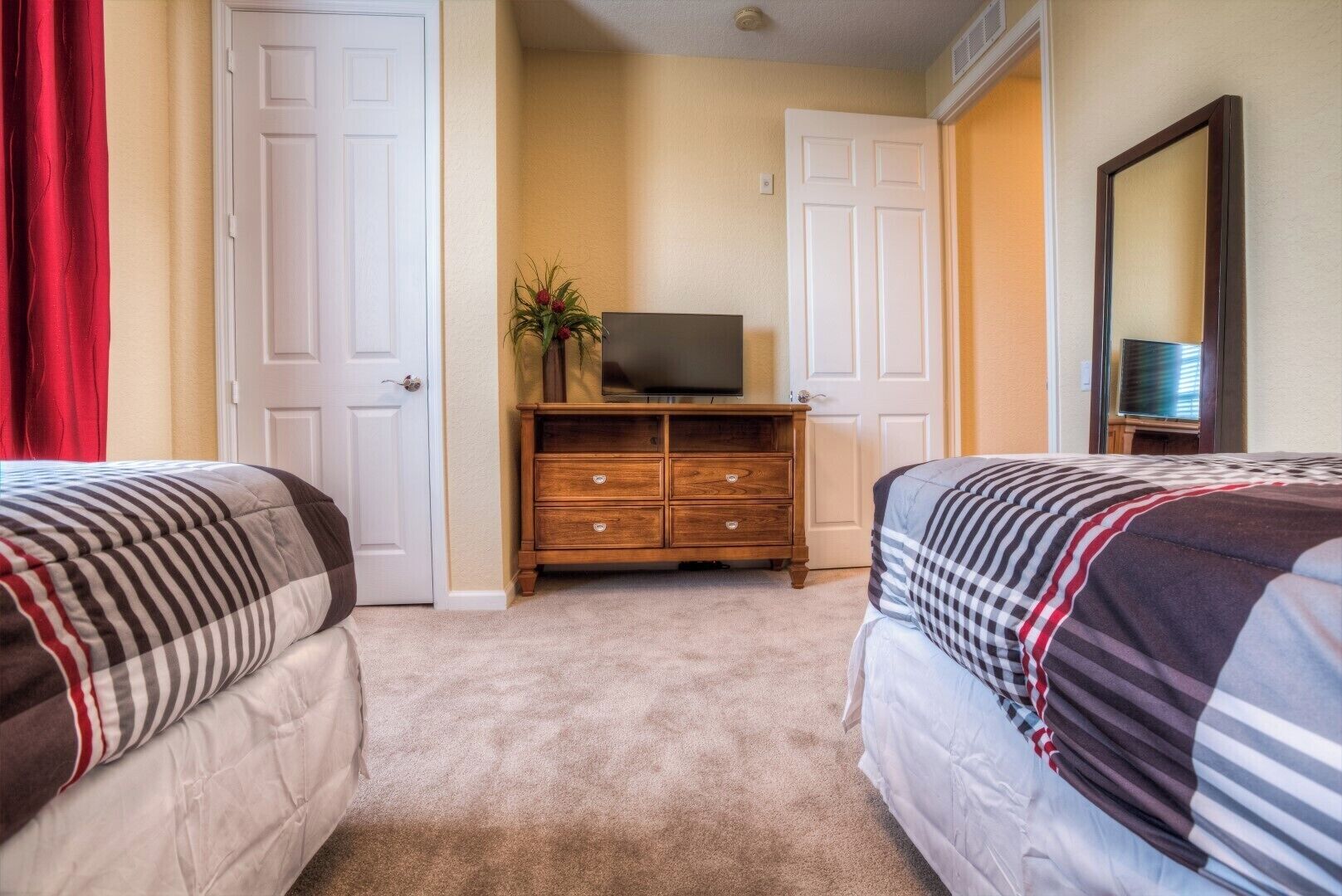A hotel room with two beds, a TV on a wooden dresser, and a mirror on the wall.