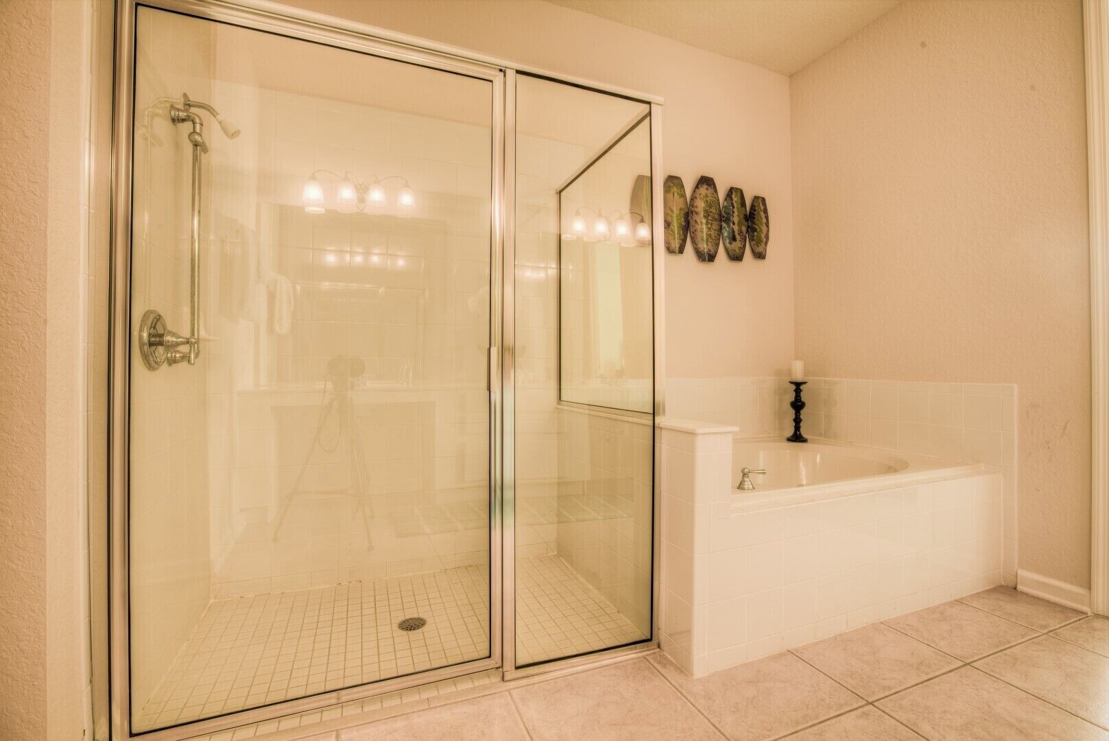 A bathroom with a glass-enclosed shower, a white bathtub, and a tiled floor.