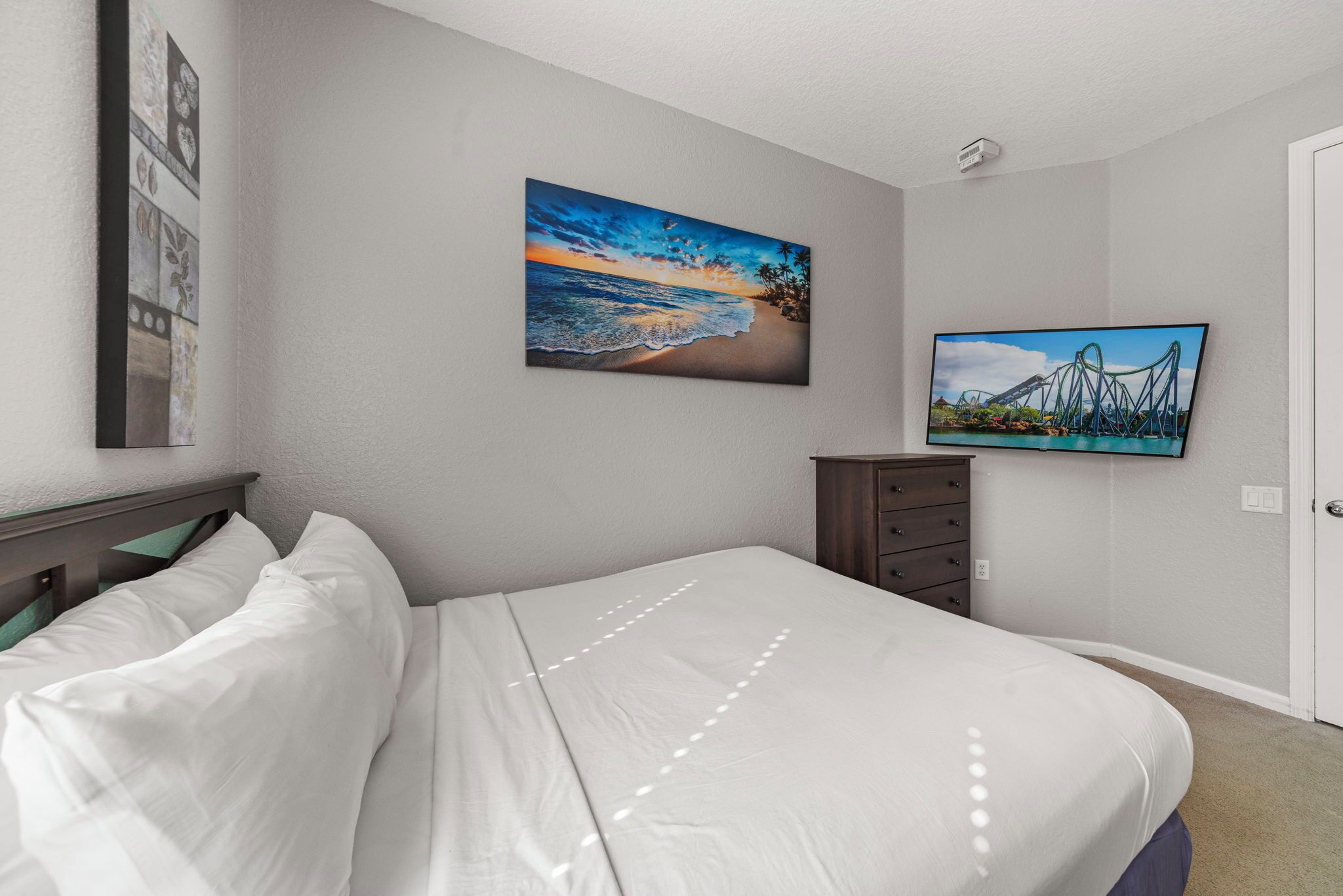 Un dormitorio con cama, mesita de noche, cómoda y dos cuadros colgados en la pared.