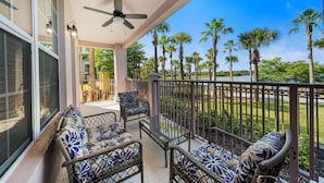A balcony with wicker furniture, a ceiling fan, and a view of palm trees. - Lakefront Luxury (Orlando)