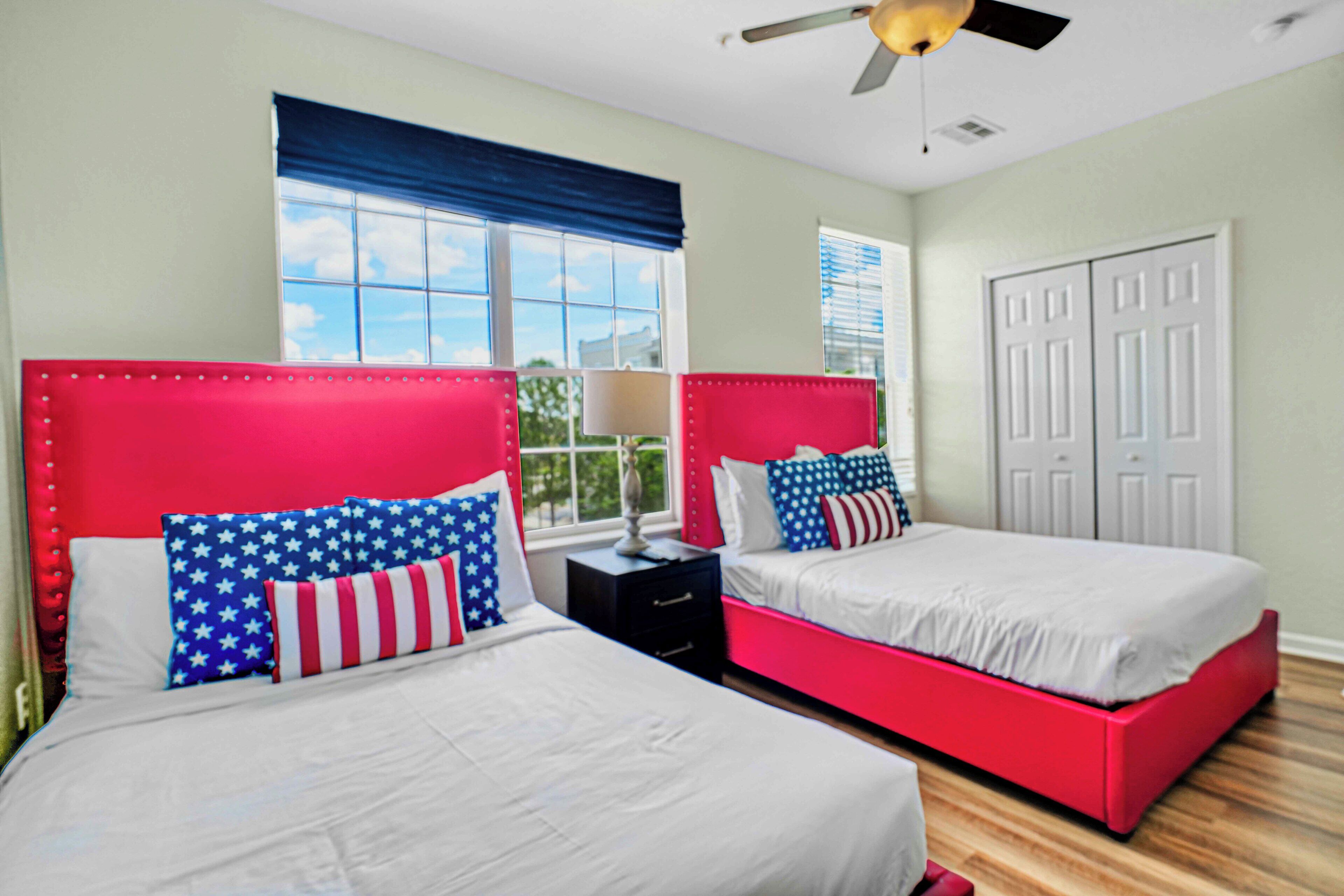 A bedroom with two beds, a ceiling fan, and a window with blinds.