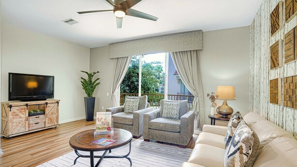 A living room with a TV, a round coffee table, two armchairs, a sofa, a ceiling fan, and a view of the outdoors through large windows. - Spacious Townhome W/patio & Garage! Sleeps10 (Orlando)