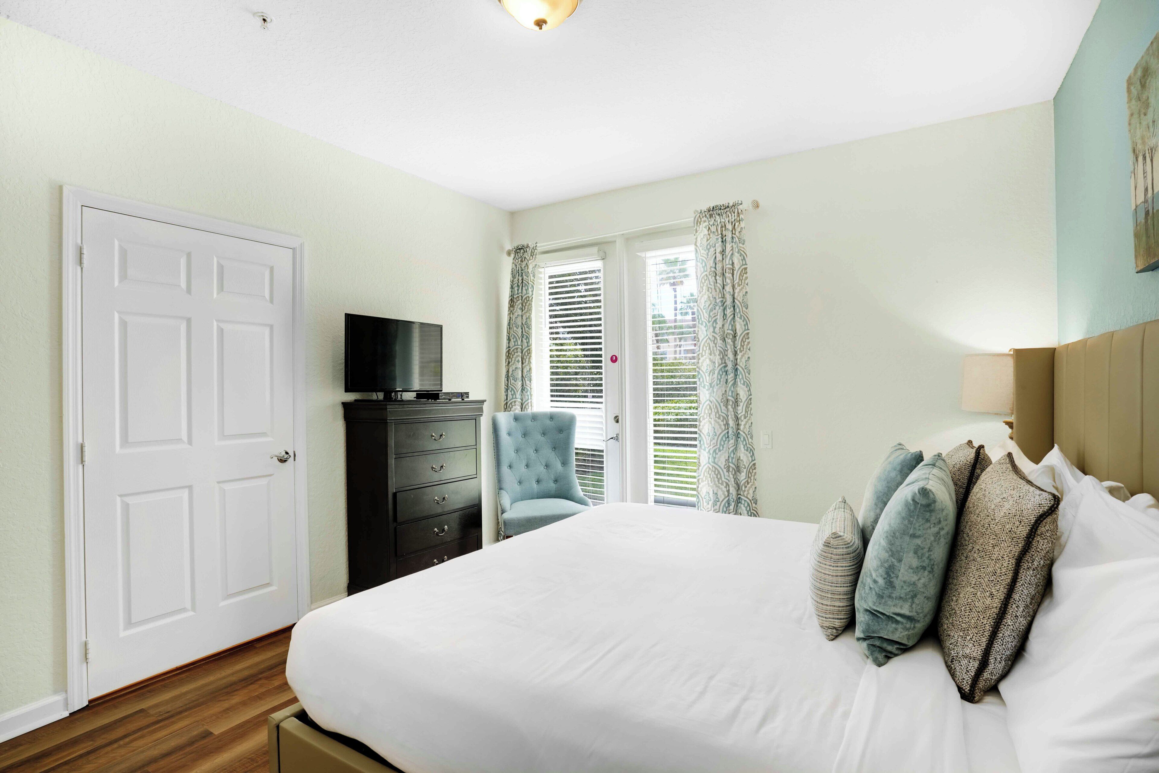 A bedroom with a bed, a dresser, a chair, and a television.