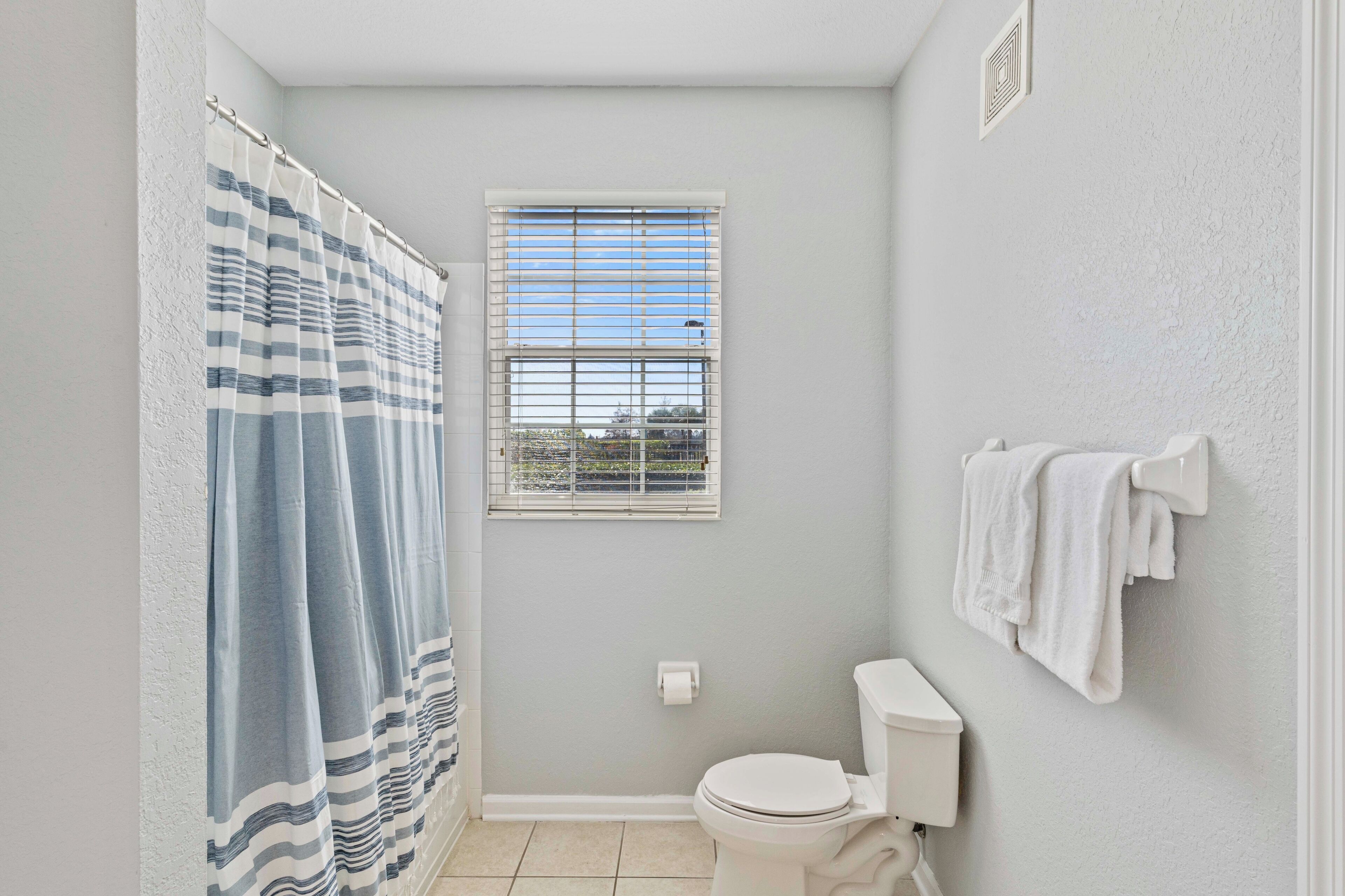 A bathroom with a shower curtain, a window, a toilet, and a towel rack.