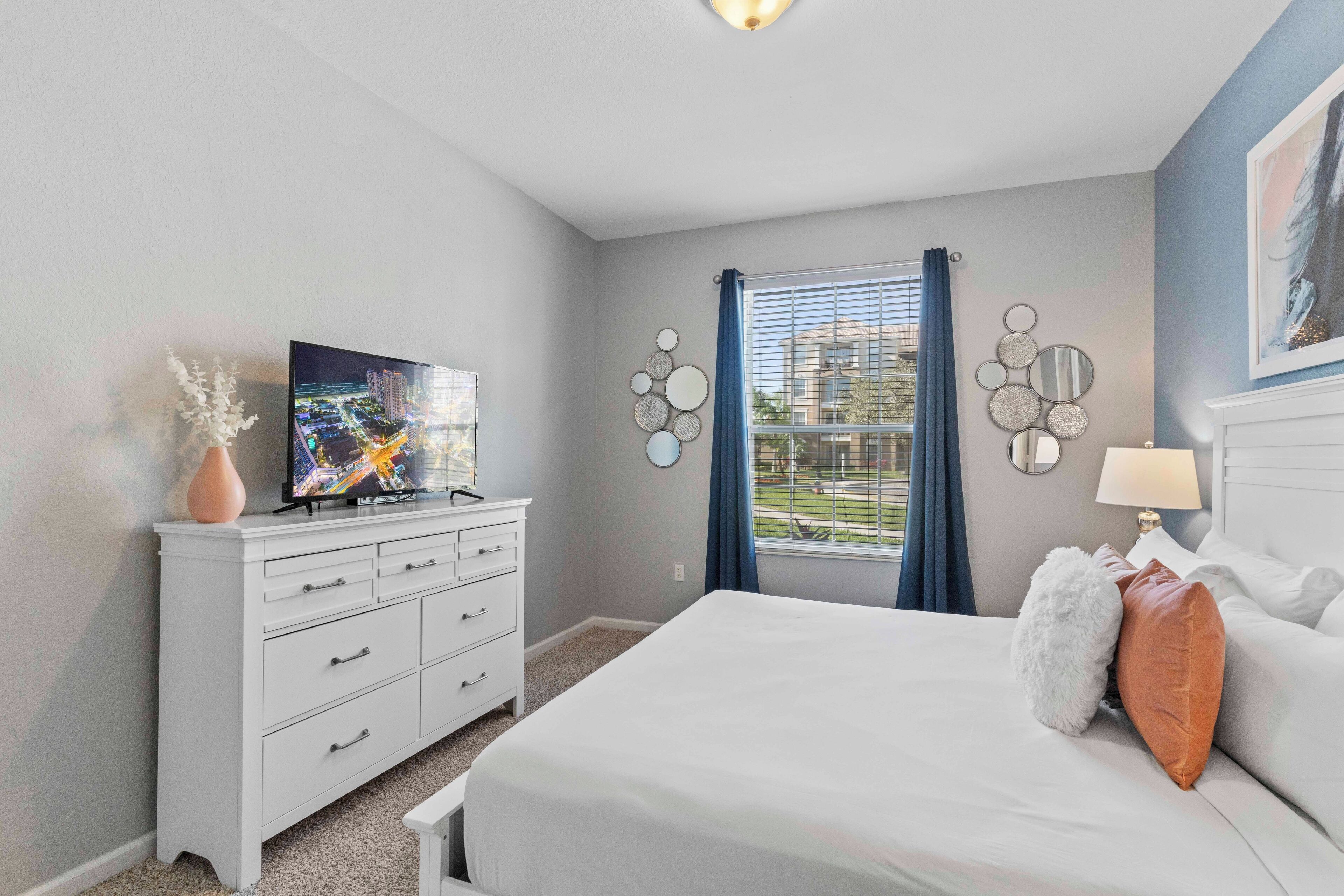 A bedroom with a bed, a dresser, a TV, and a window with curtains.