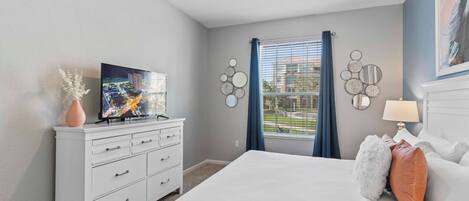 A bedroom with a bed, a dresser, a TV, and a window with curtains.