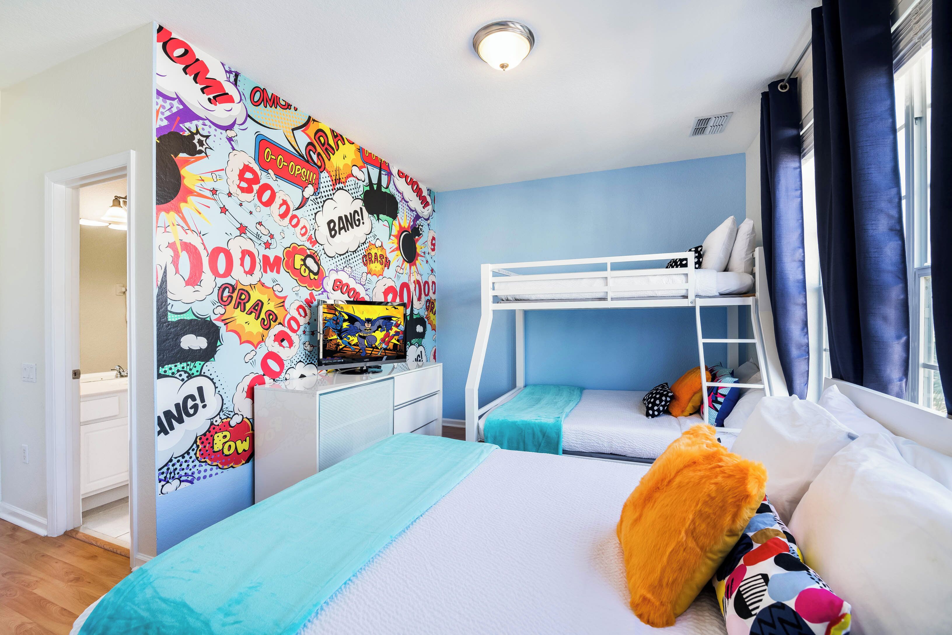 Una habitación con literas, un mural de estilo cómic muy colorido, un televisor y una ventana con cortinas.