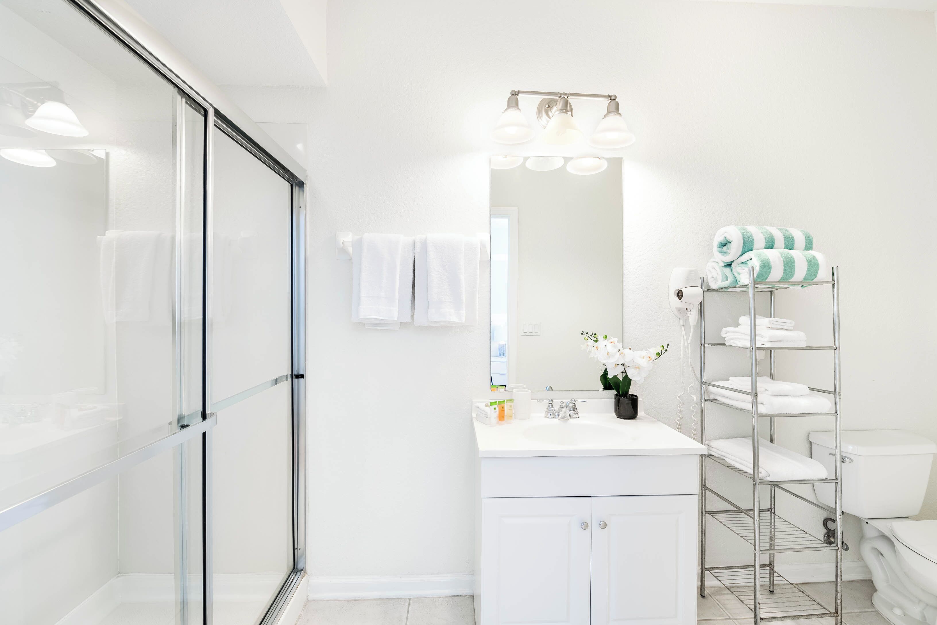 A modern bathroom with a glass shower enclosure, a white vanity with a mirror, and a towel rack with neatly folded towels.