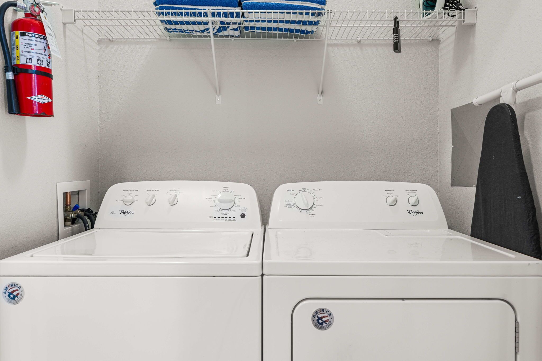 Un espace buanderie comprenant deux machines à laver à chargement frontal, un extincteur et une étagère avec des serviettes.