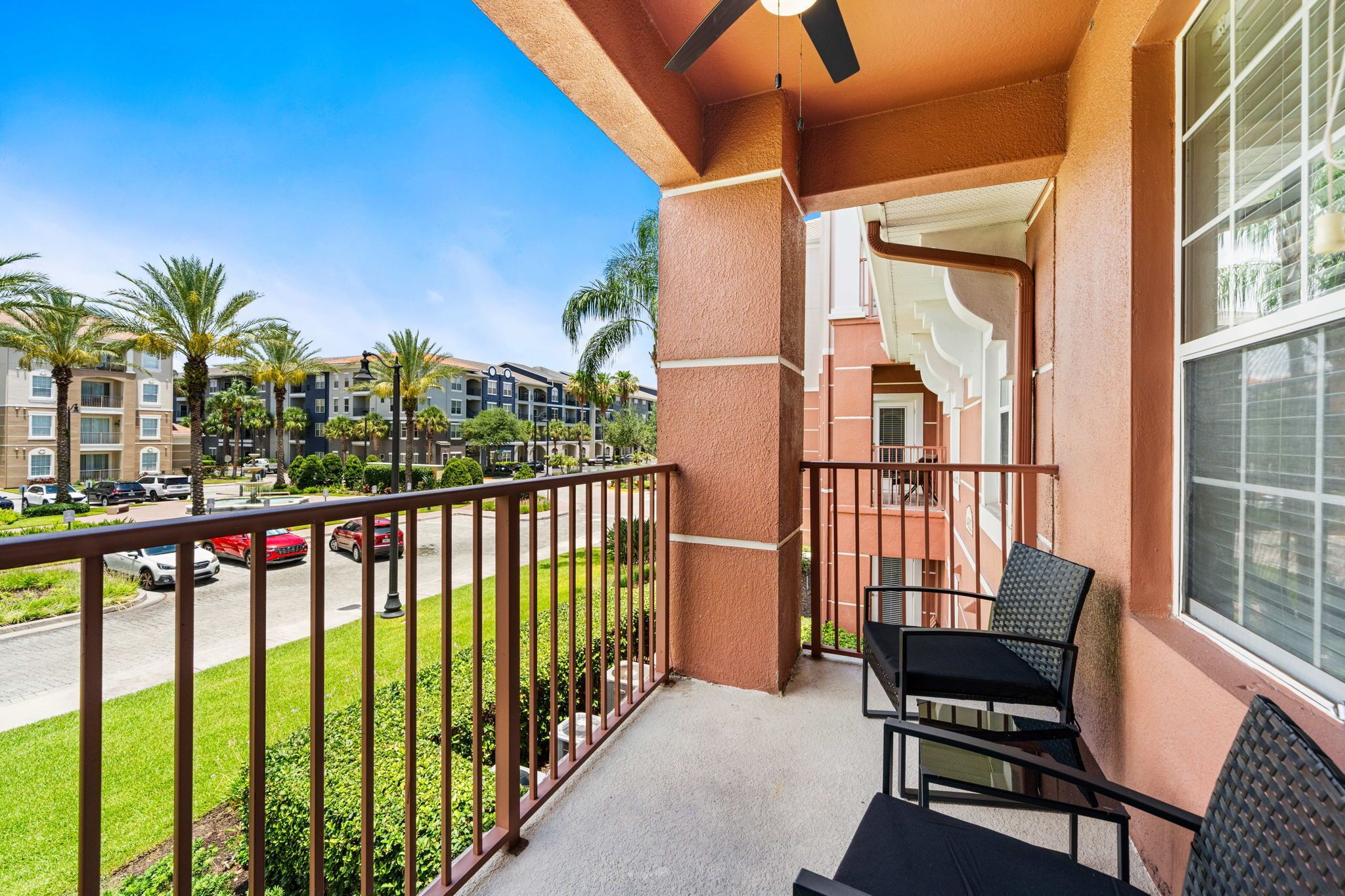 A balcony with a view of a parking lot and buildings, a ceiling fan, and outdoor furniture.