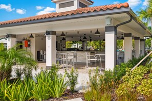 An outdoor patio area with a covered seating area, a kitchen counter, and a staircase leading to an upper level.