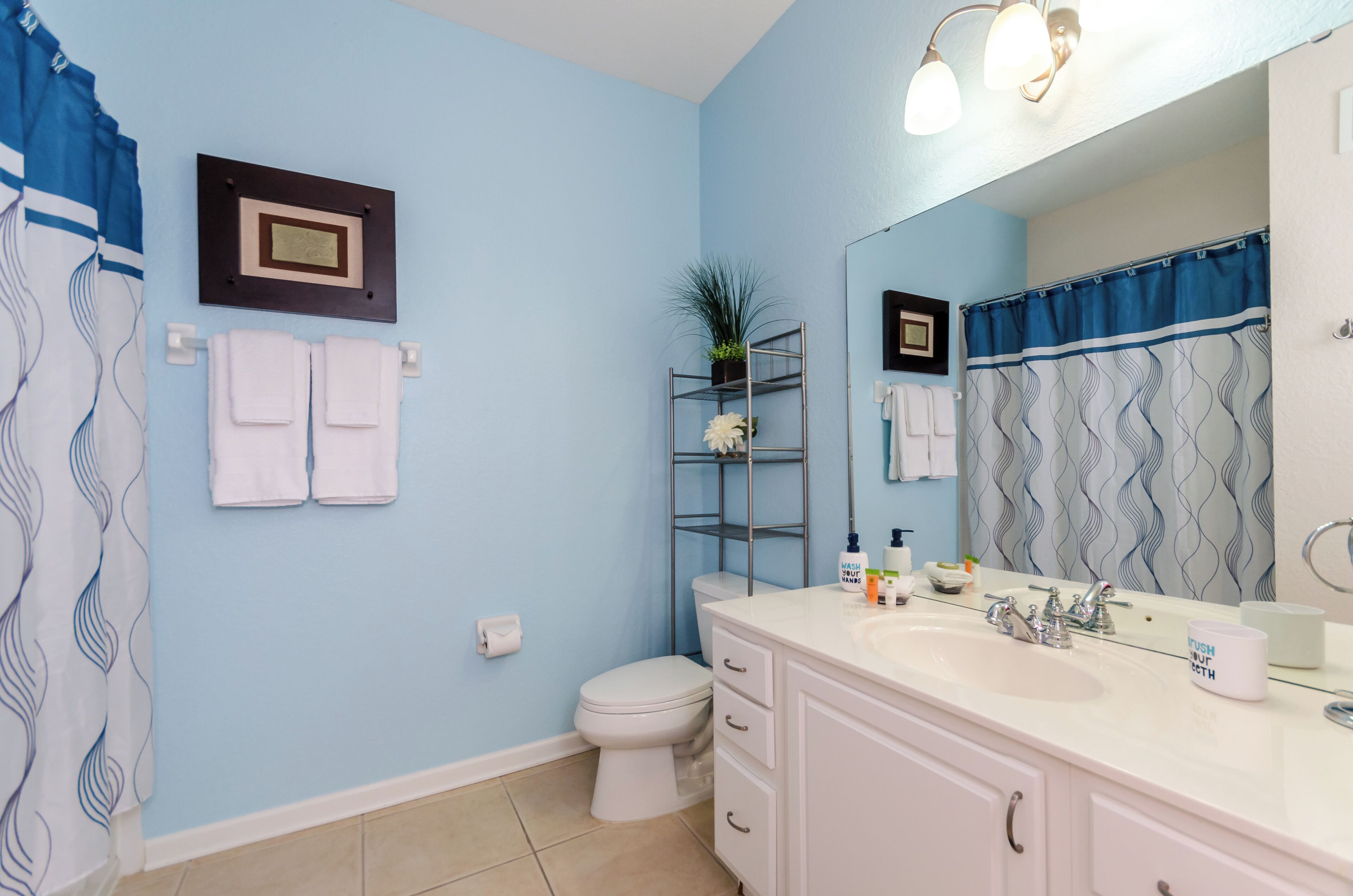 A bathroom with a blue wall, white fixtures, a white sink, and a shower curtain with a wavy pattern.