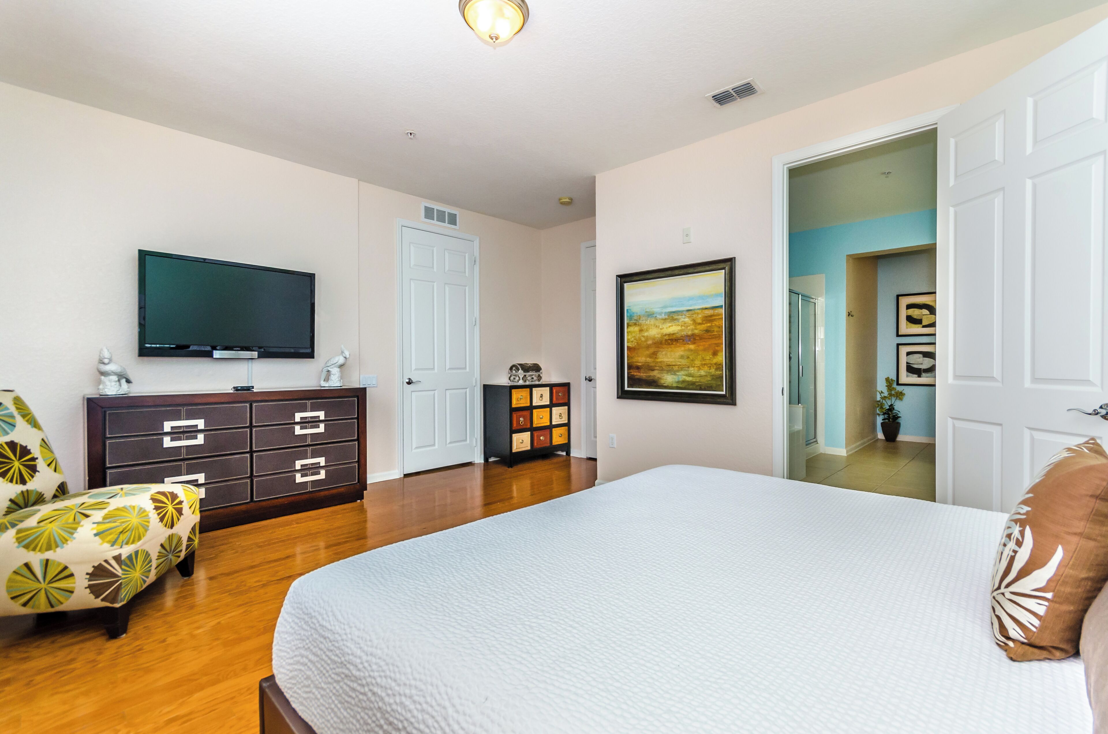 A bedroom with a large bed, a dresser, a television, and a chair.