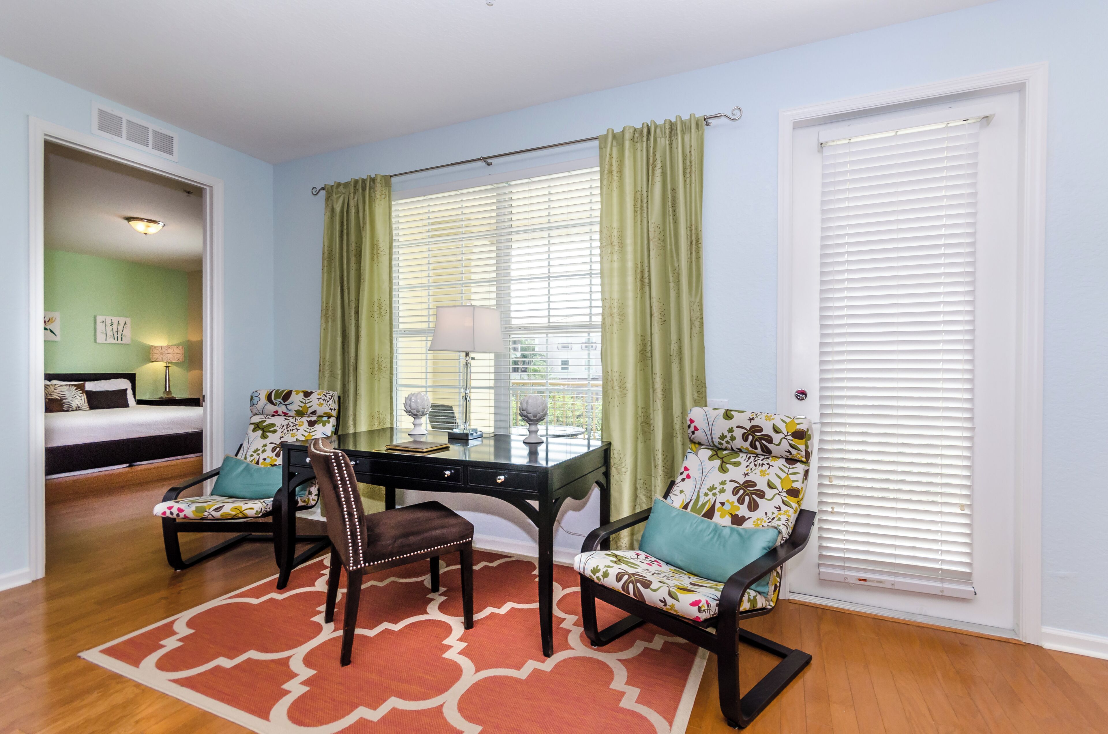A room with a desk, two chairs, a bed, and a window with curtains.