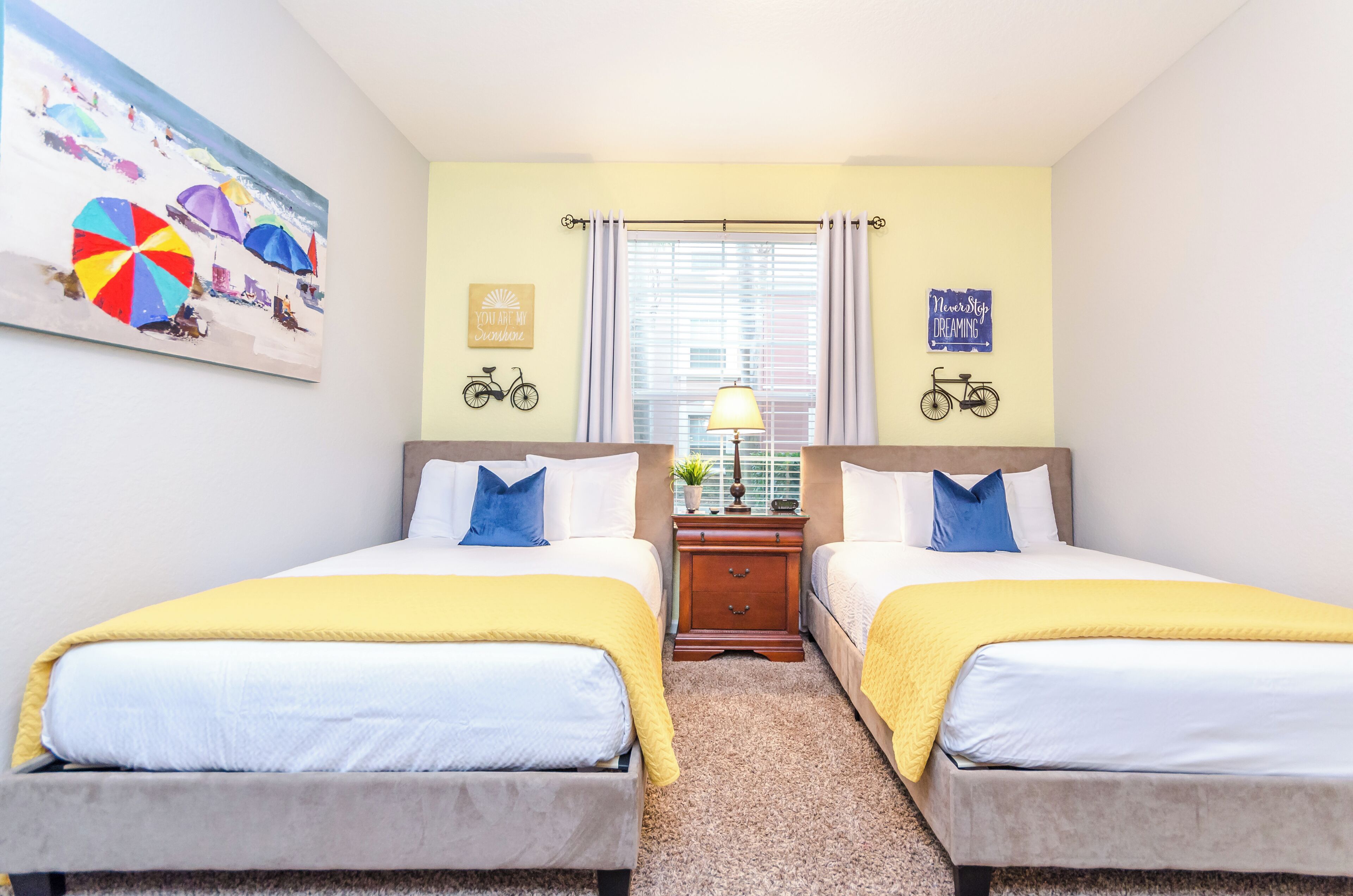 A hotel room with two beds, a painting of beach umbrellas, and motivational wall art.