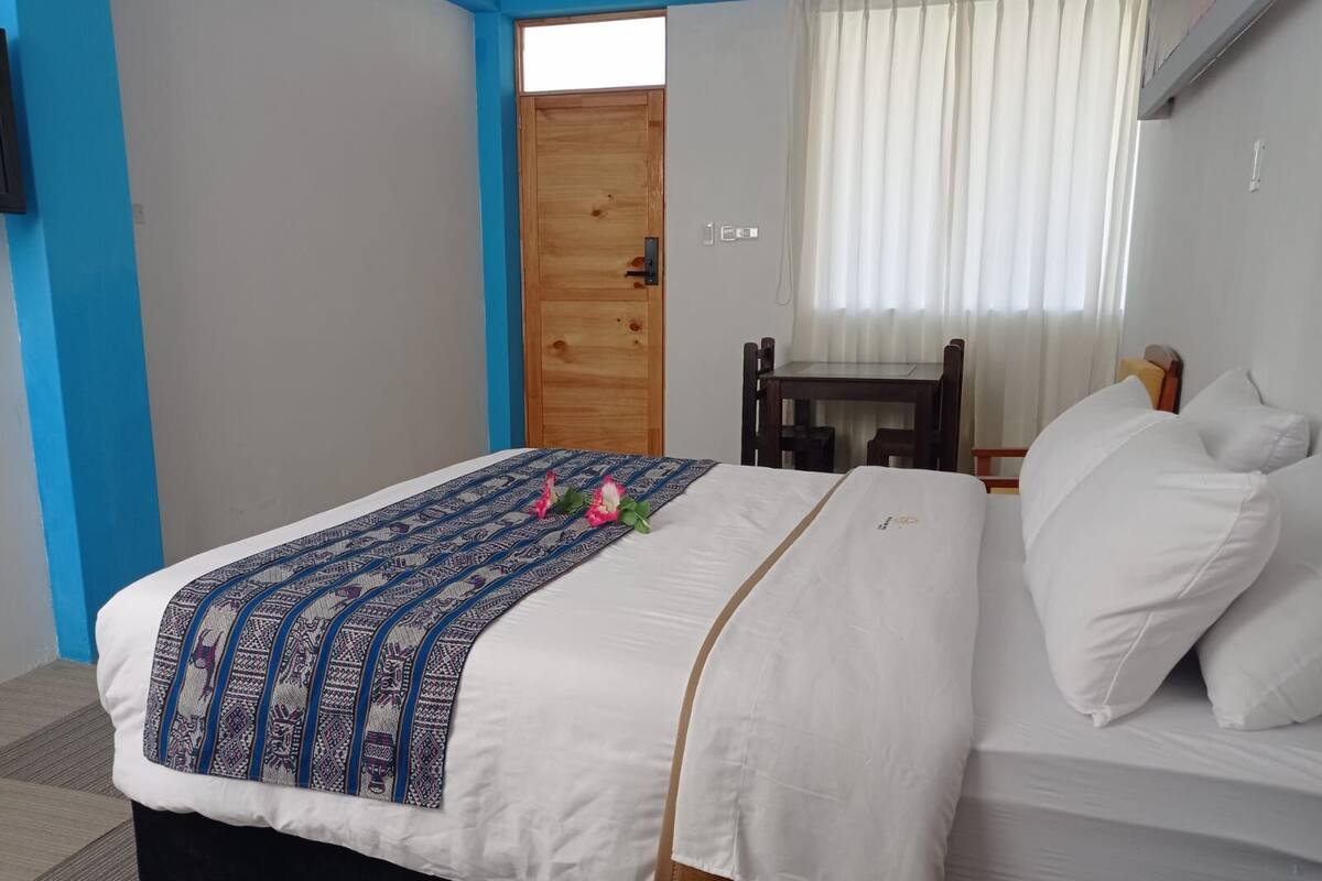 Une chambre à coucher avec un lit, une porte en bois, une petite table et une fenêtre avec des rideaux.